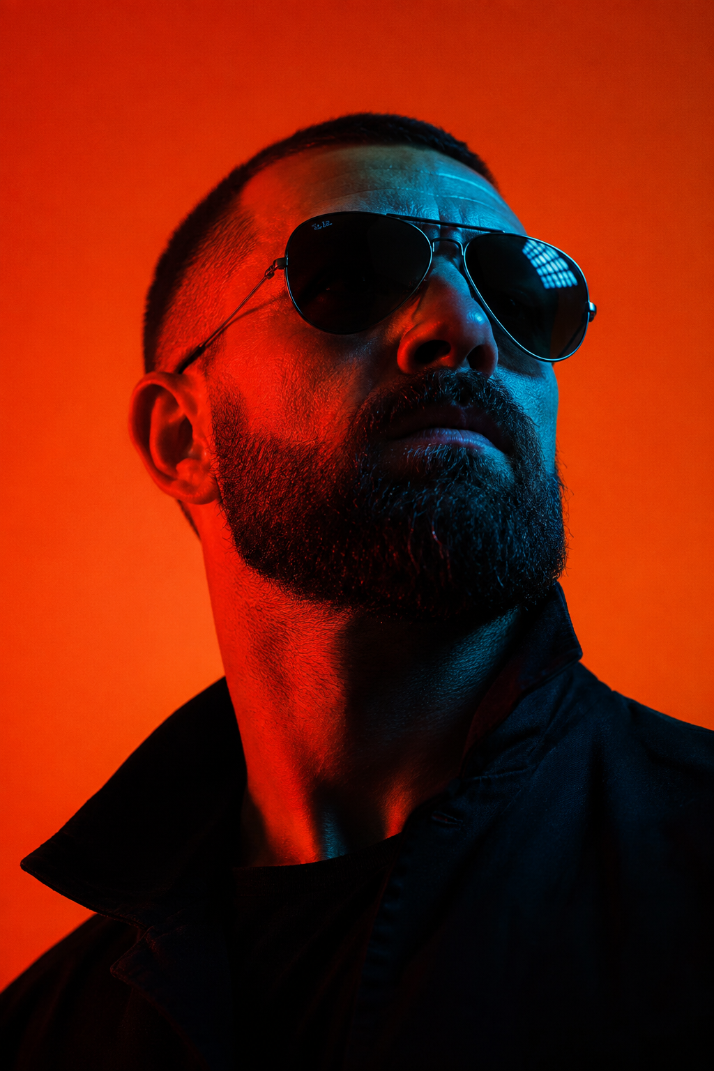 Portrait of a man with sunglasses and a beard, illuminated by red and blue lighting.