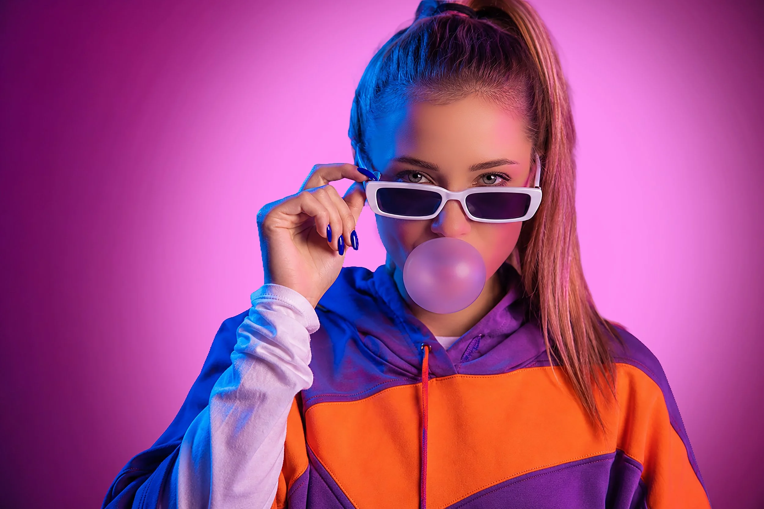 A young woman with braided hair wearing white sunglasses, a purple and orange jacket, and blowing a bubblegum bubble against a pink background.