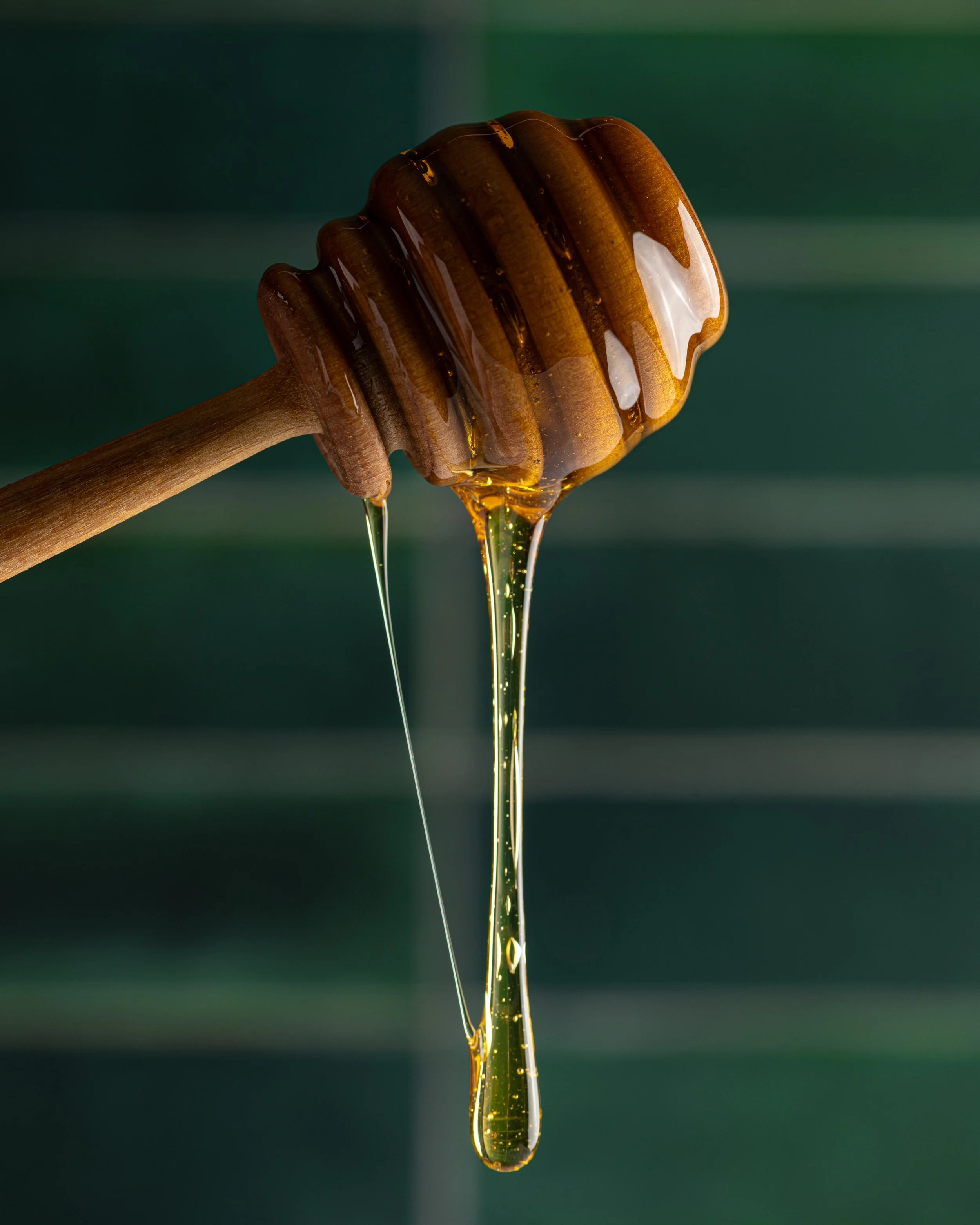 Close-up of honey dripping from a wooden honey dipper.