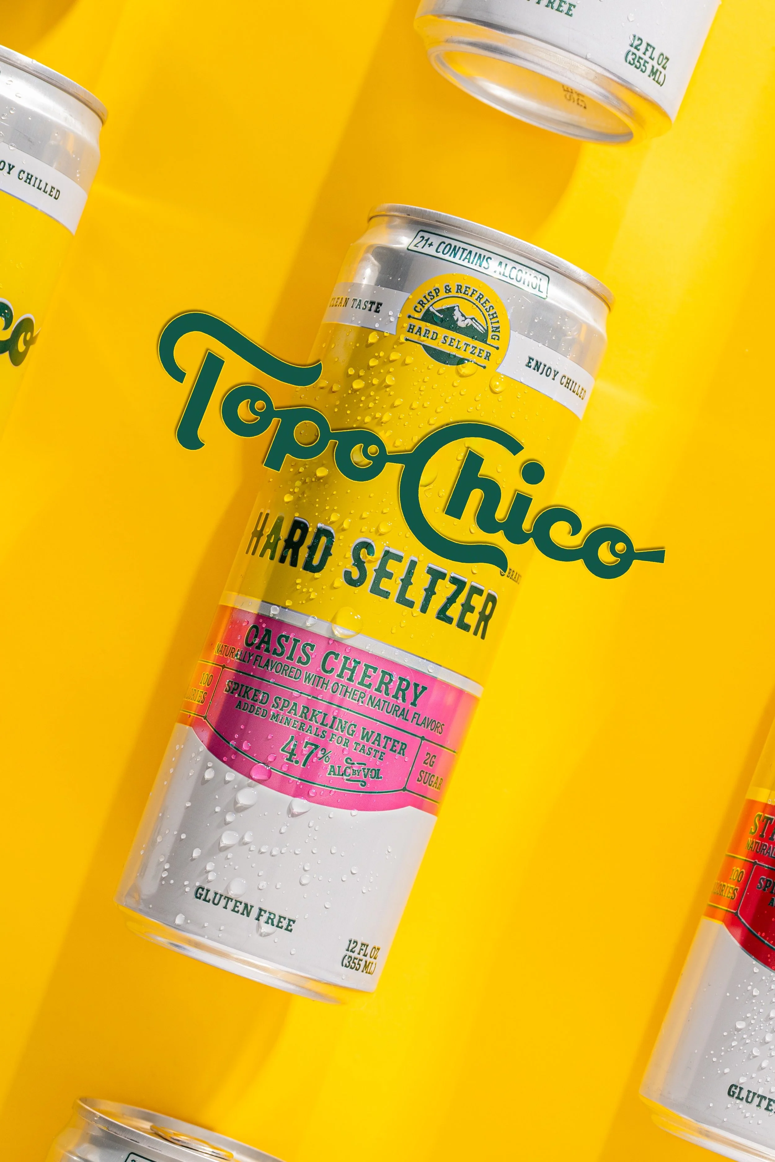 Multiple cans of Topo Chico hard seltzer with lemon flavor placed on a bright yellow background. The cans are covered with condensation, and the product label features a mountain logo with text indicating gluten-free, natural flavors, and 4.7% alcoho