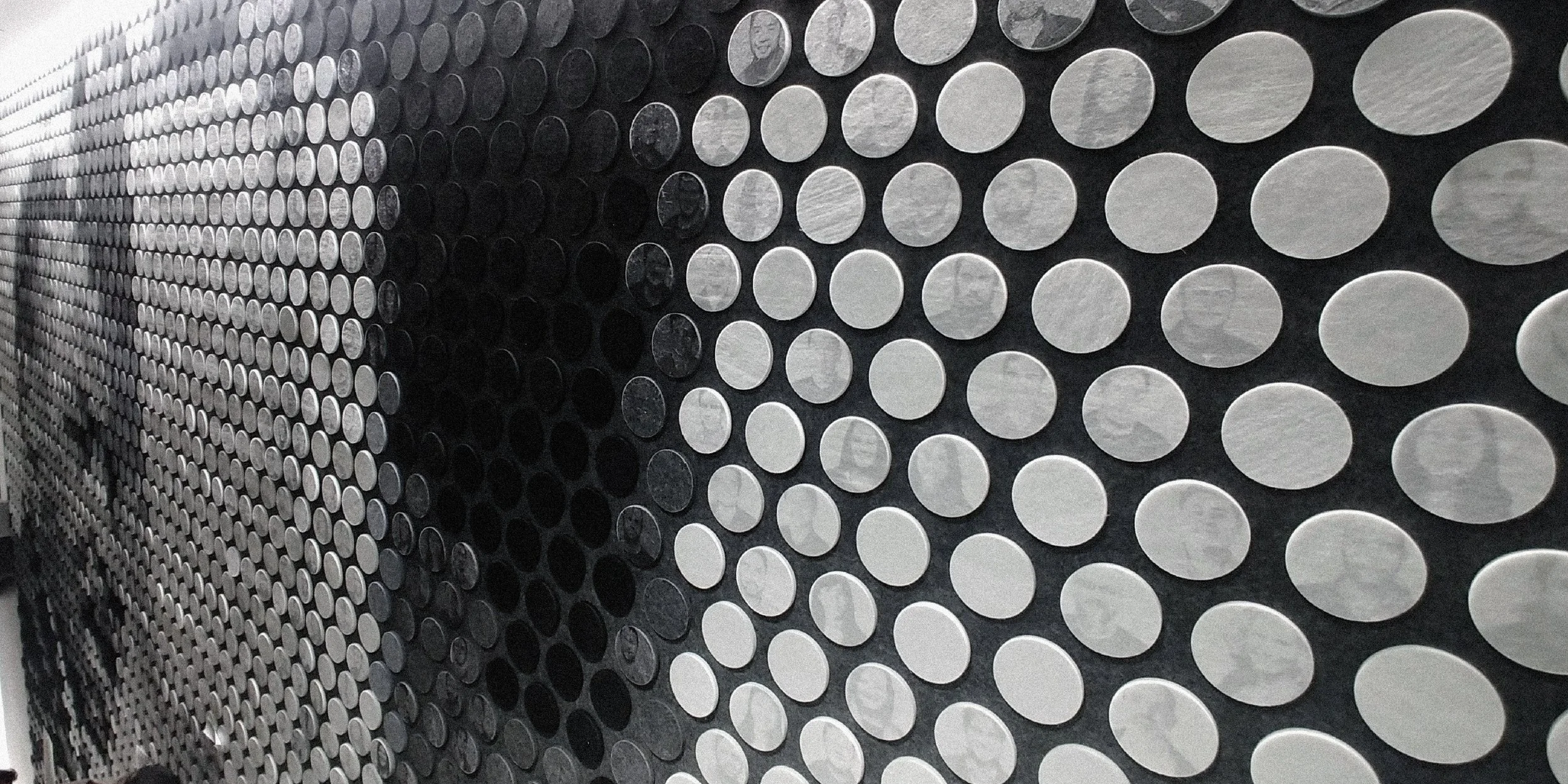 Wall installation composed of numerous circular discs arranged in a grid pattern, featuring alternating black and white discs.
