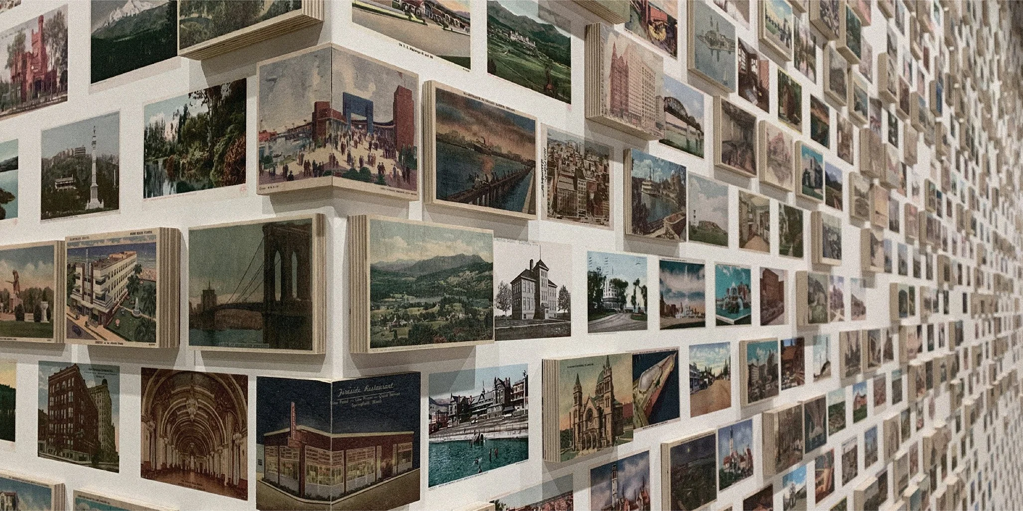 A wall covered with numerous small postcards or photographs arranged in a grid, showcasing various cityscapes, landmarks, and scenic locations.