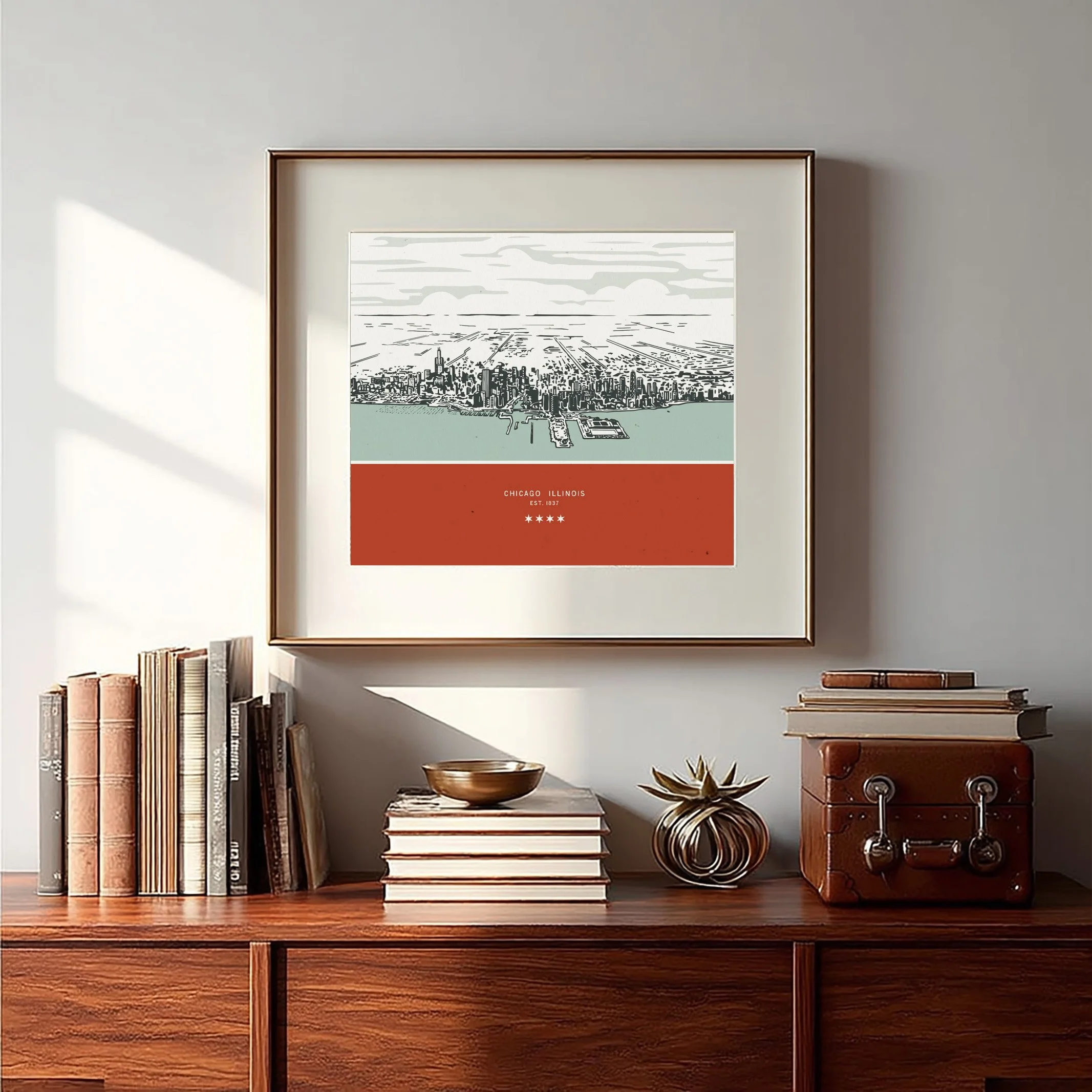 Decorative framed cityscape map of Chicago Illinois hanging on a white wall, with books and decorative objects on a wooden sideboard below.