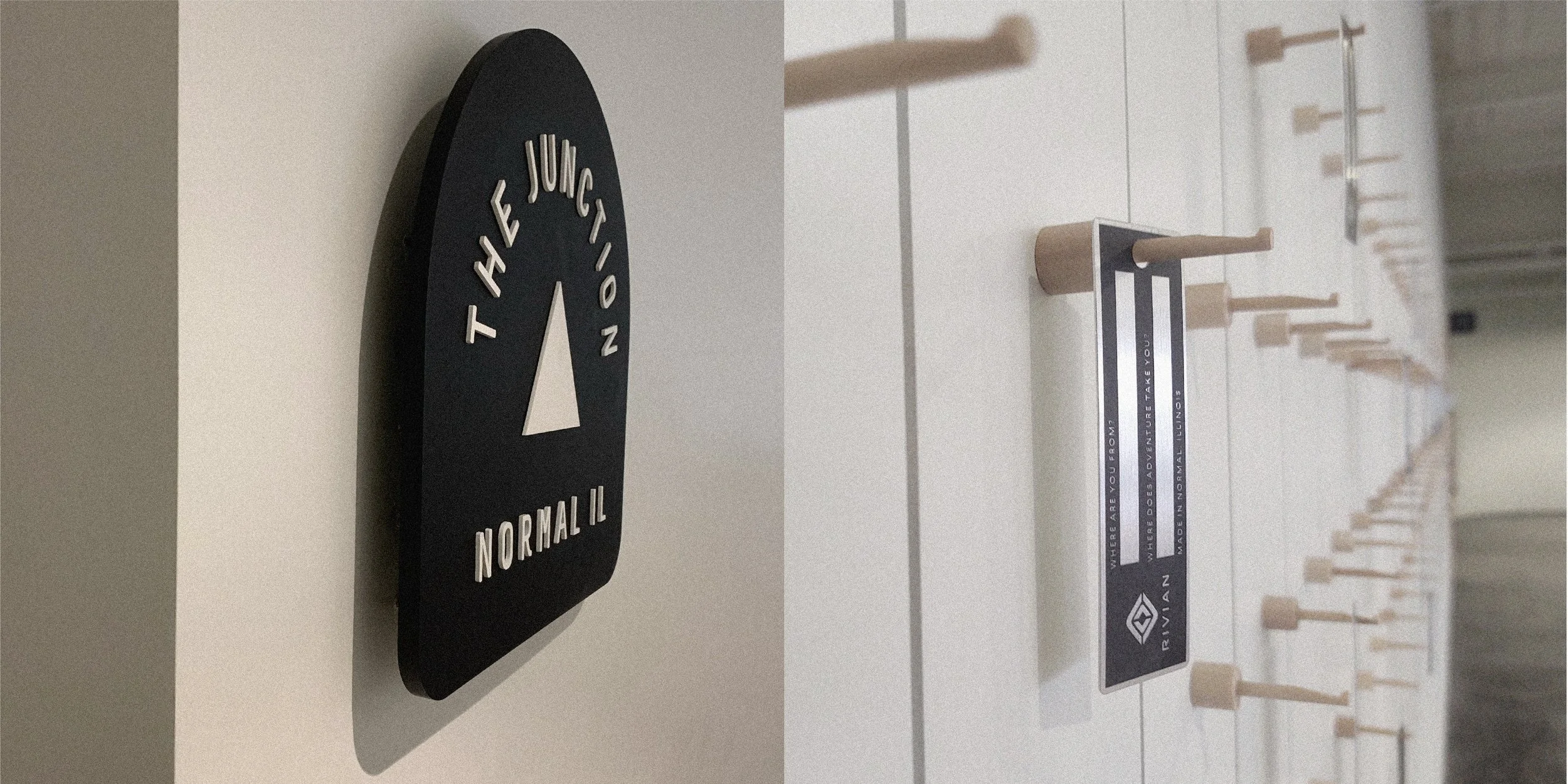 Close-up view of a black, oval-shaped sign with a white arrow in the center and the phrase 'The Junction' above, and the word 'Normal IL' below. The sign is mounted on a white wall.