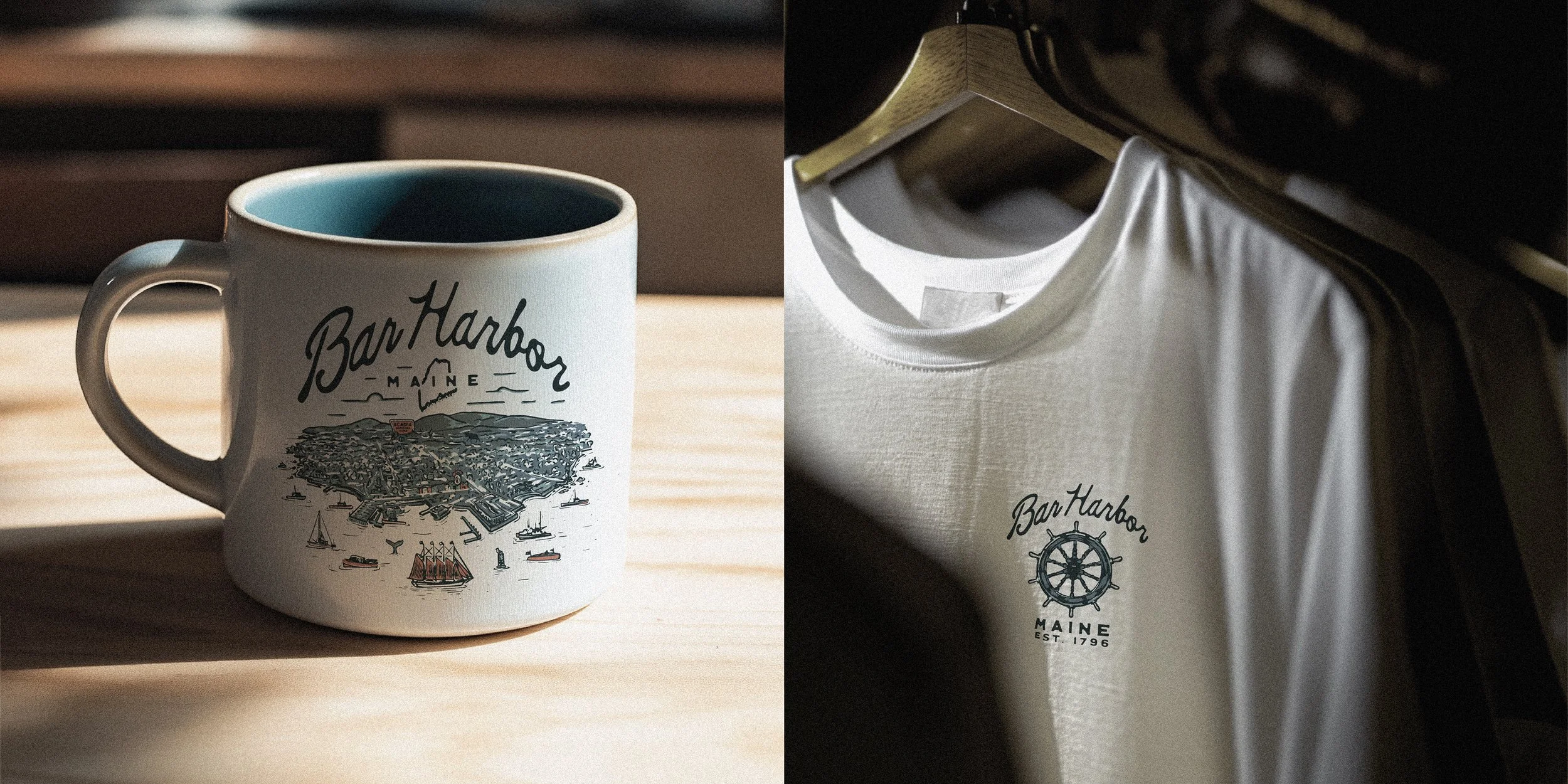 A white mug with a Maine map and sailboats design and a white T-shirt with a similar design hanging on a wooden hanger, both featuring the text "Bar Harbor Maine est. 1796."