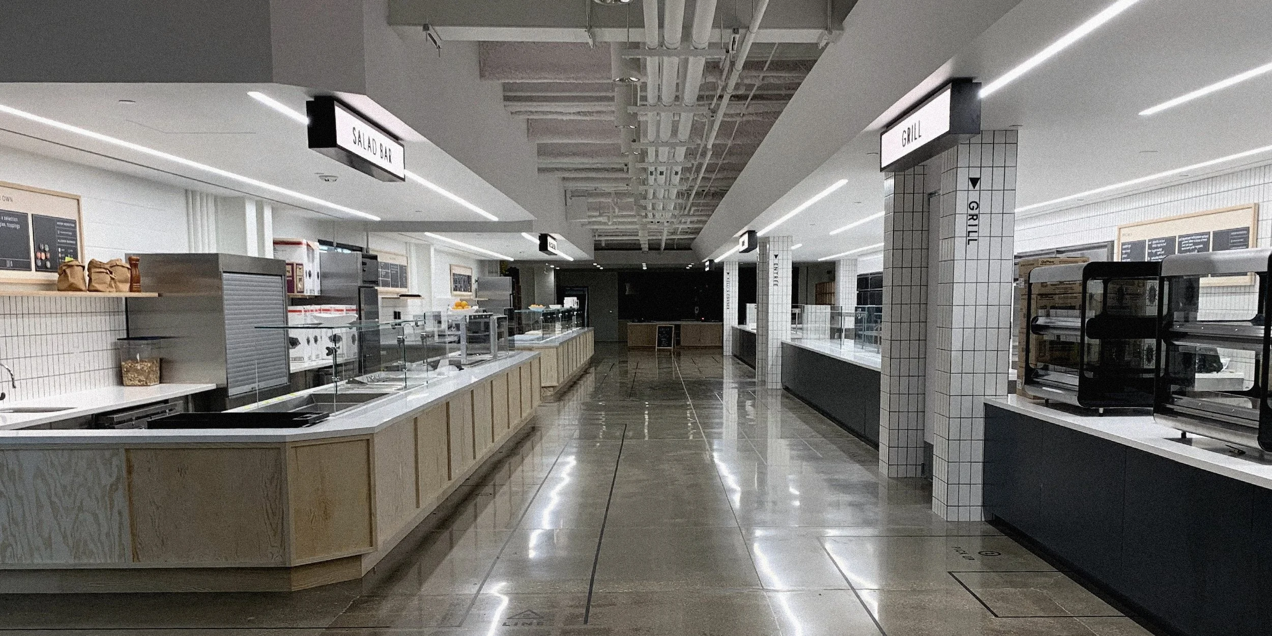 Empty cafeteria with modern design, food counters, and signage for salad bar and grill.