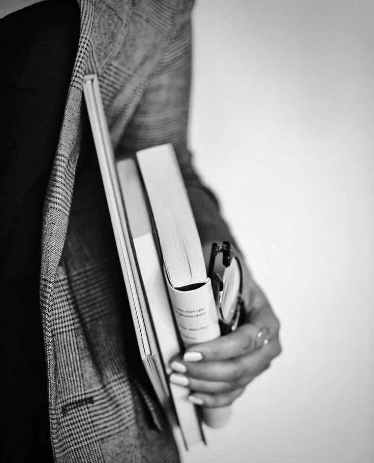 Person holding notebooks, a rolled-up document, and a pen, dressed in business attire.