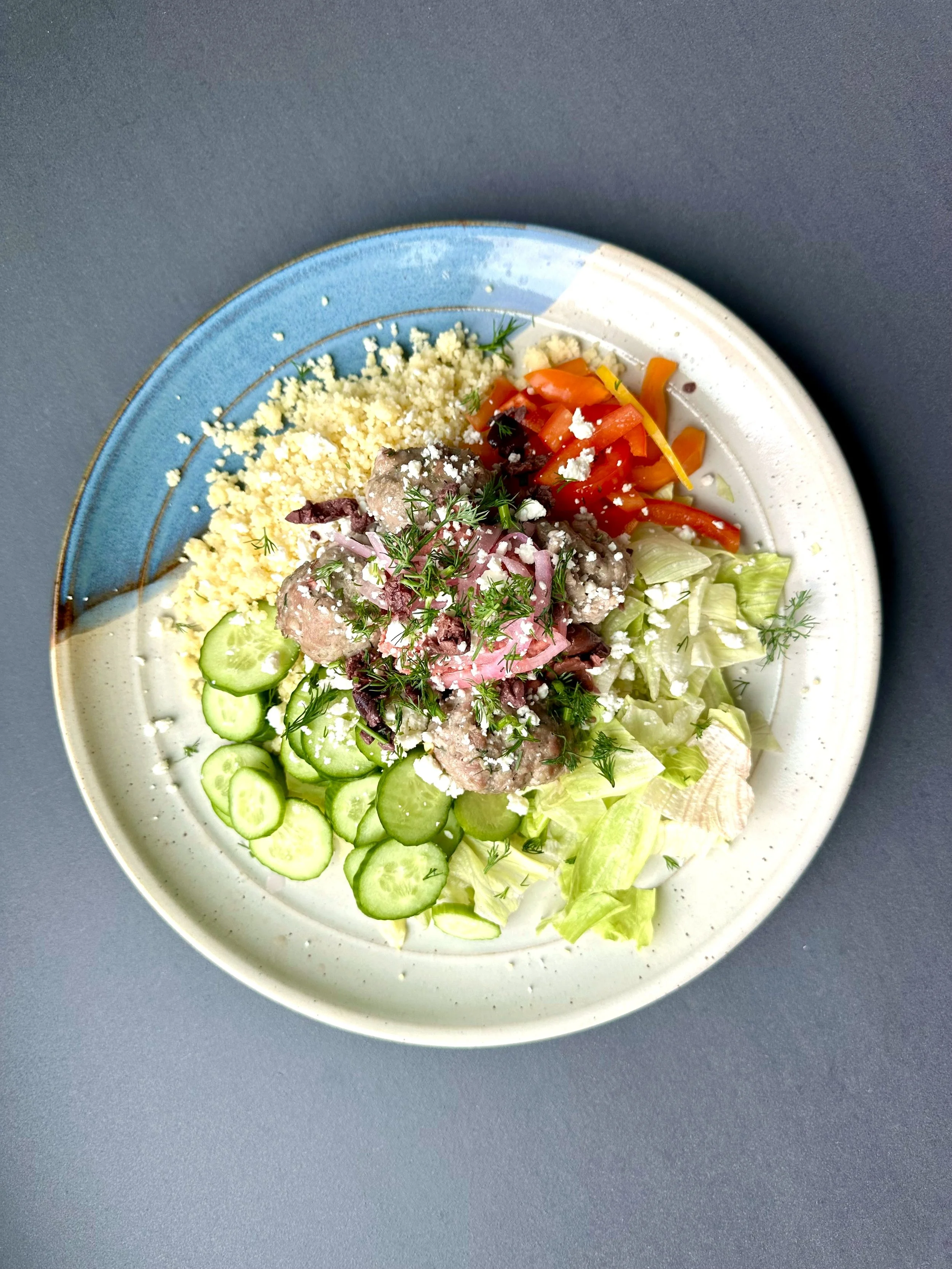 A plate of salad with cucumber, lettuce, cherry tomatoes, shredded carrots, crumbled cheese, and garnished with herbs.
