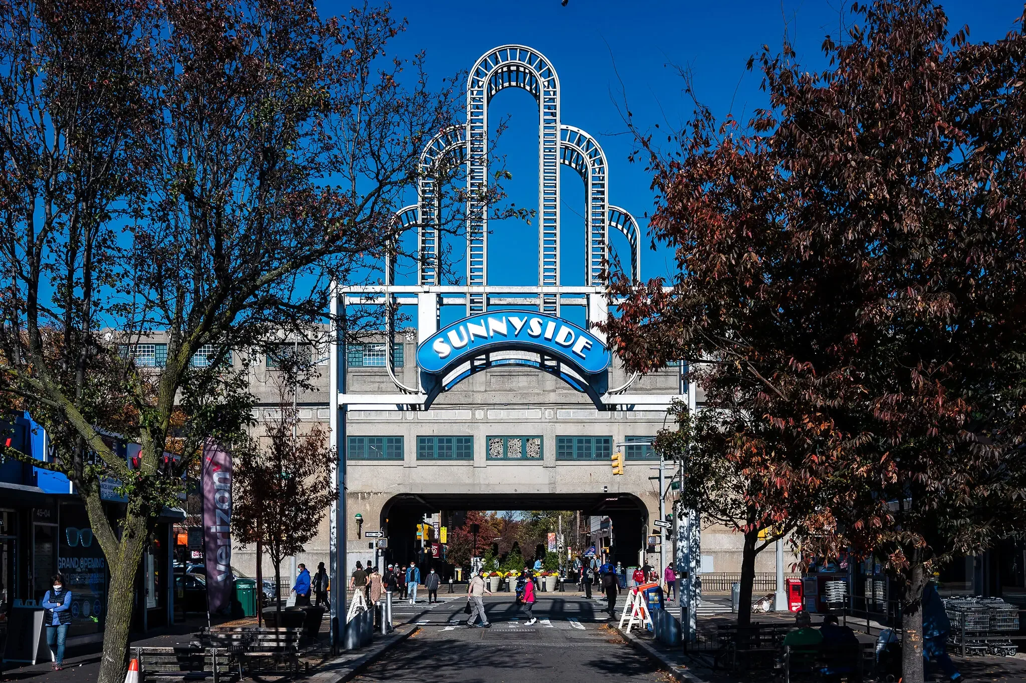 Sunnyside arch- a large sign and decorative arches, trees on the sides, and people crossing the street.