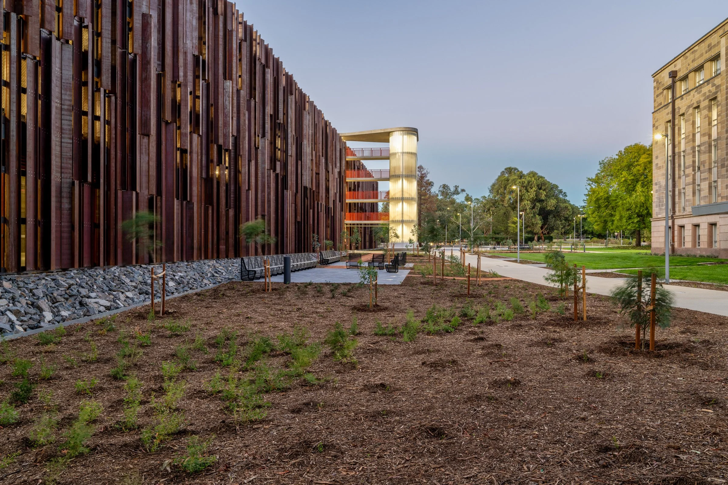 Entrance area of a modern apartment complex with a gated entry and landscaped garden, featuring a sign that says 'Main Entry' and another sign that reads 'Oaks Canopy'.