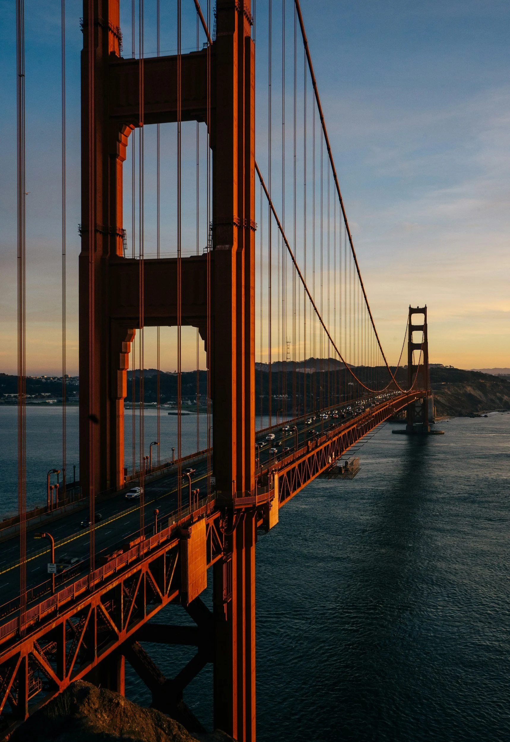 Golden Gate Bridge at sunset with cars traveling across it over the water and hills in the background.