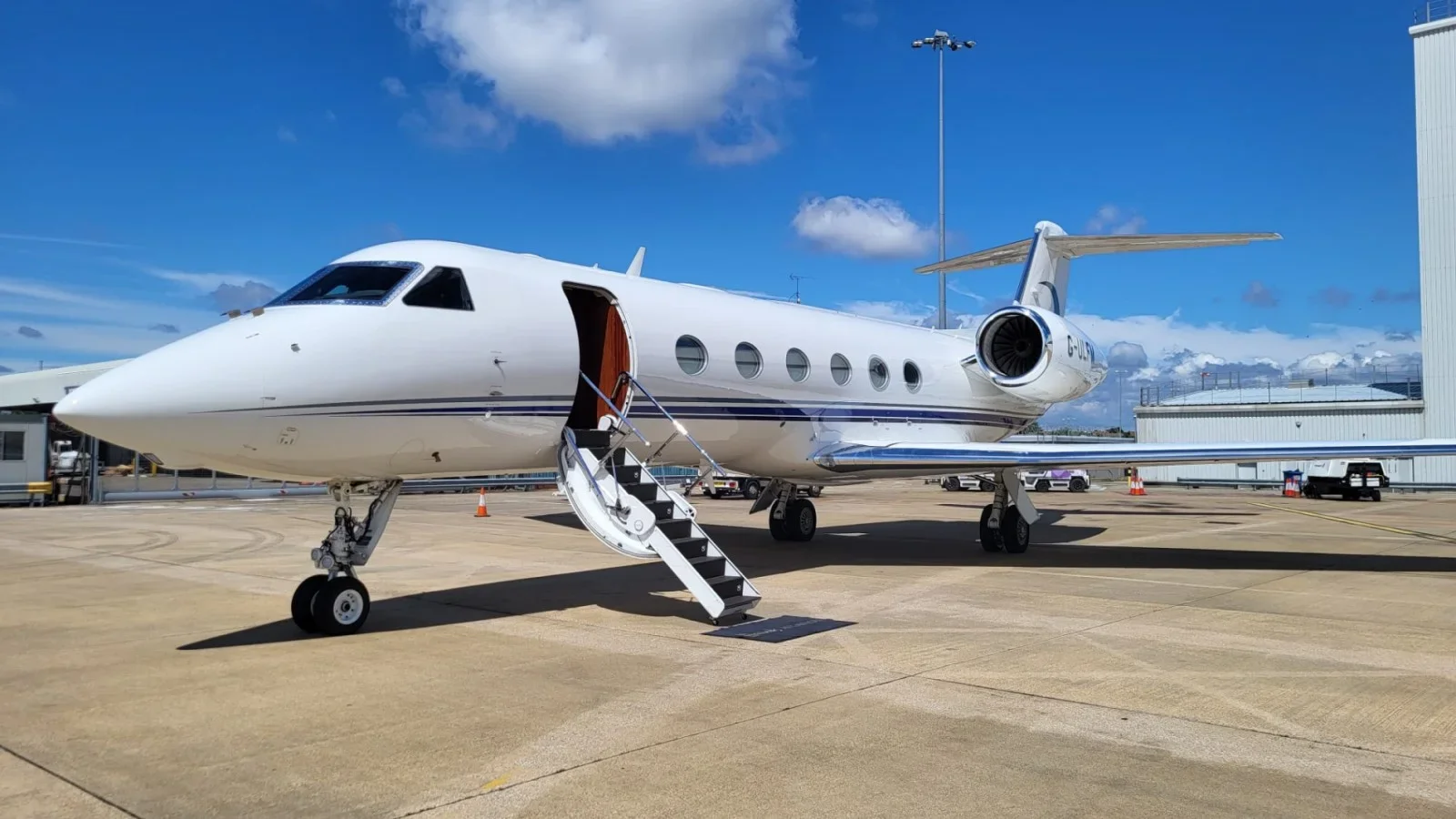 White private jet with open door and stairs on an airport tarmac, under a partly cloudy sky.