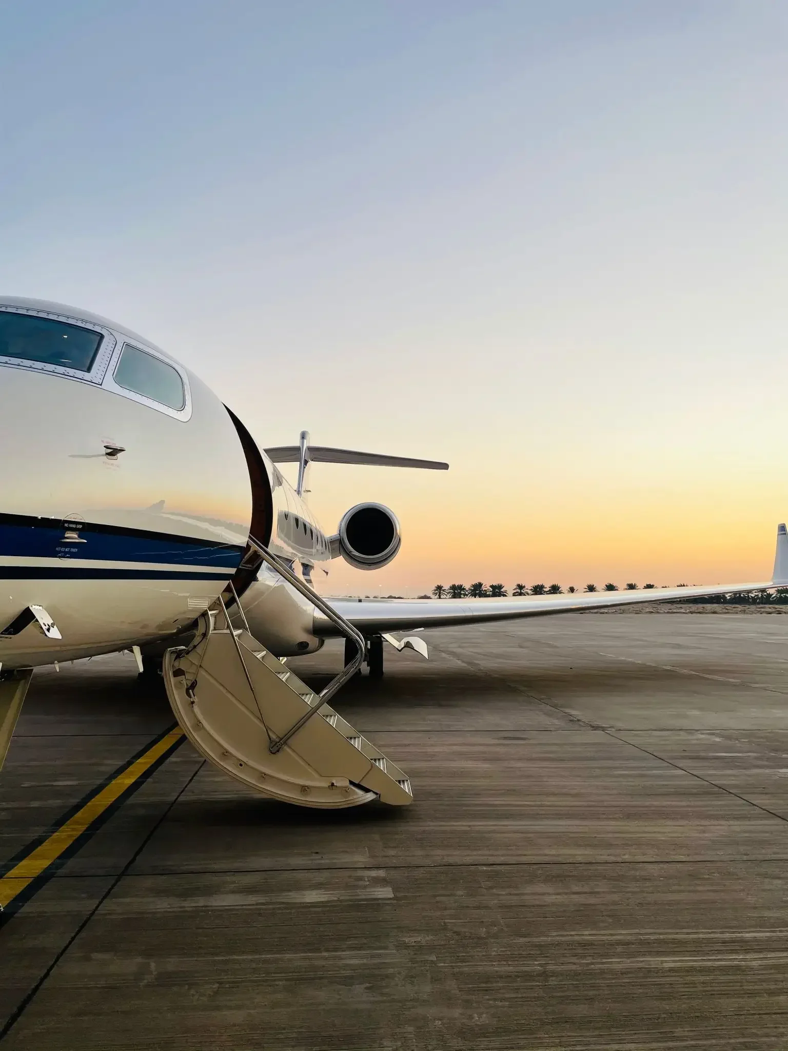 A private jet parked on the tarmac during sunset, with stairs leading to the entrance.