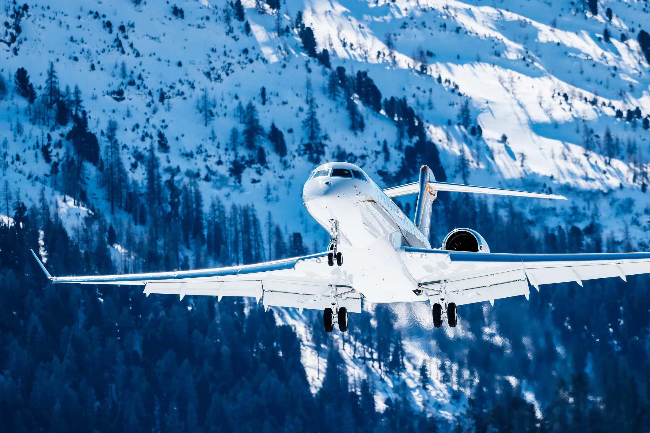 A white commercial airplane flying over snow-covered mountains with trees.