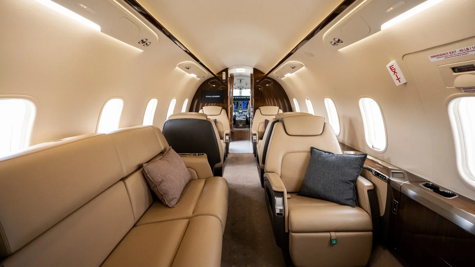 Interior of a private jet with beige leather seats, small pillows, and an aisle leading to the cockpit.