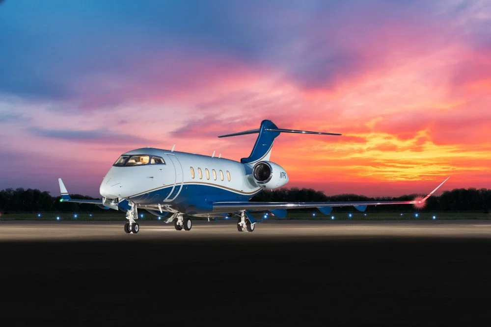 A private jet parked on an airport runway during a colorful sunset with pink, purple, and orange sky.