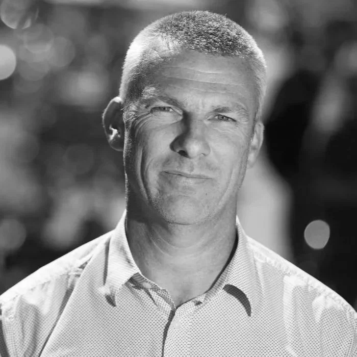 Black and white photo of a man with short hair, wearing a collared shirt, looking at the camera with a slight smile.