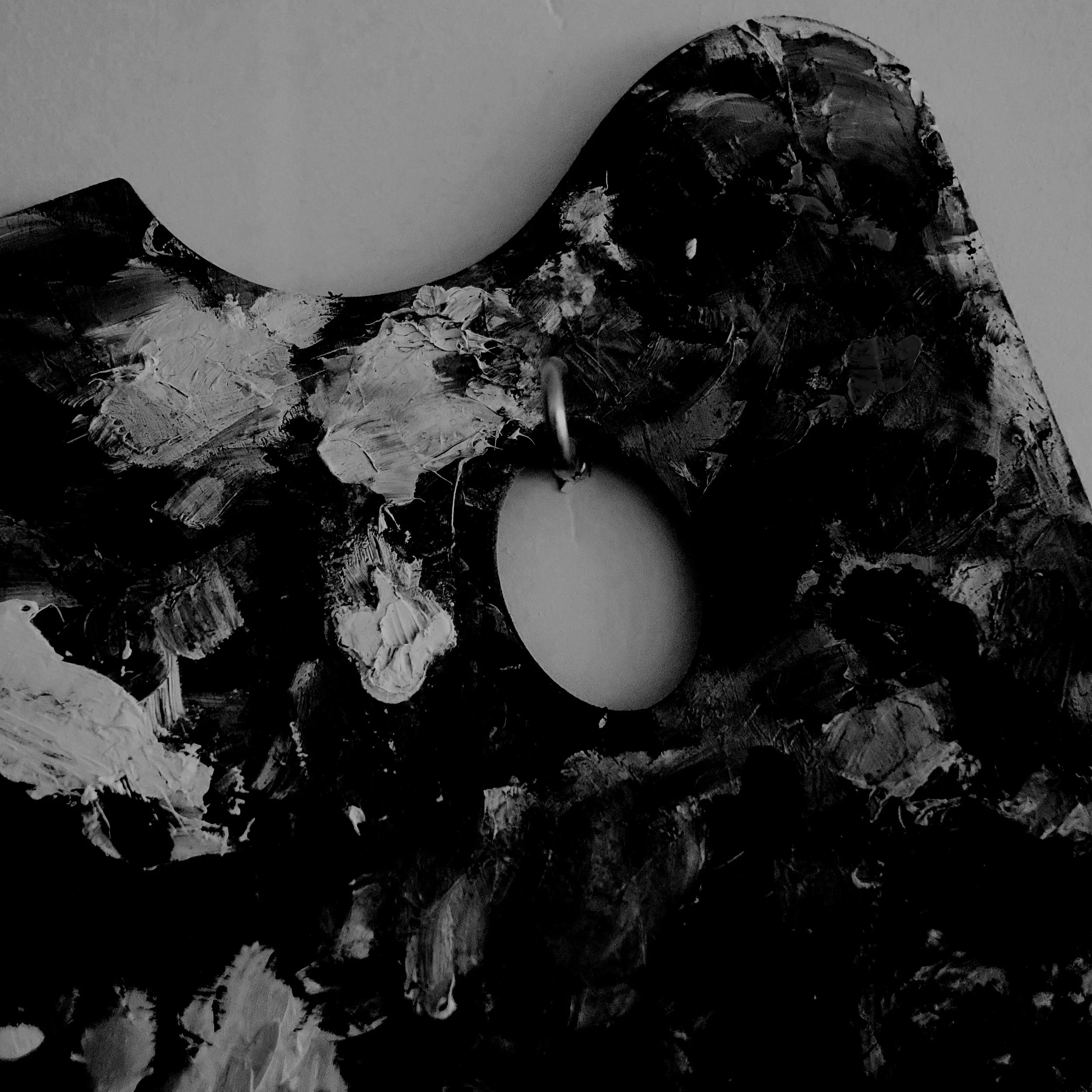 Close-up of a textured abstract painting in black and white with thick, uneven brushstrokes, featuring a circular cutout or hole at the center.