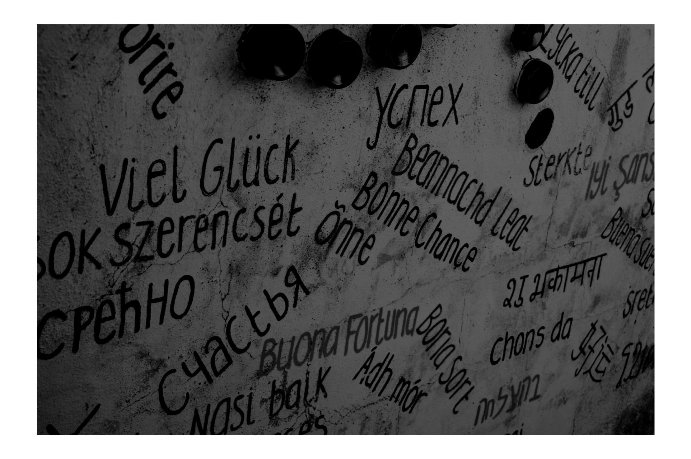 Wall with various words of congratulations, luck, and success in multiple languages, along with small black decorative objects.