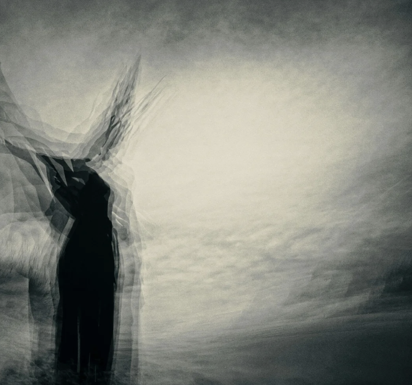 A black silhouette of a person walking with a large, blurred silhouette of a deer next to them against a cloudy sky with a bright light