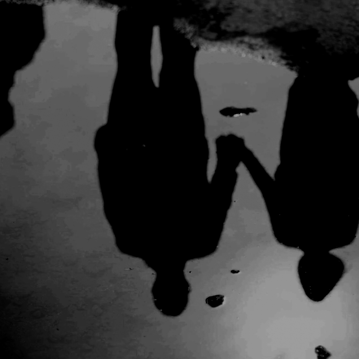 Silhouettes of a parent and child holding hands reflected in a puddle of water on the ground.