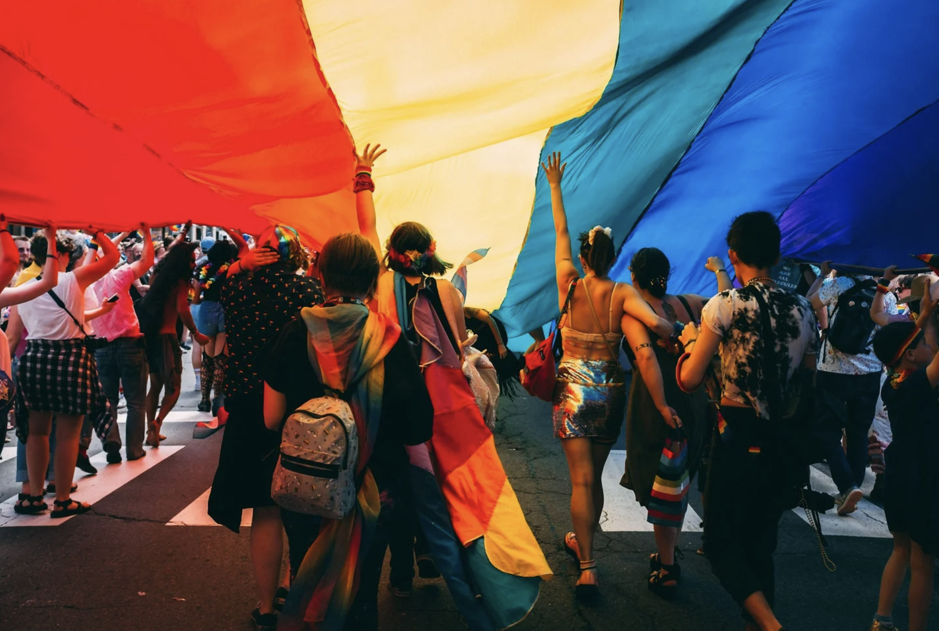 People participating in a Pride parade, holding a large rainbow flag overhead