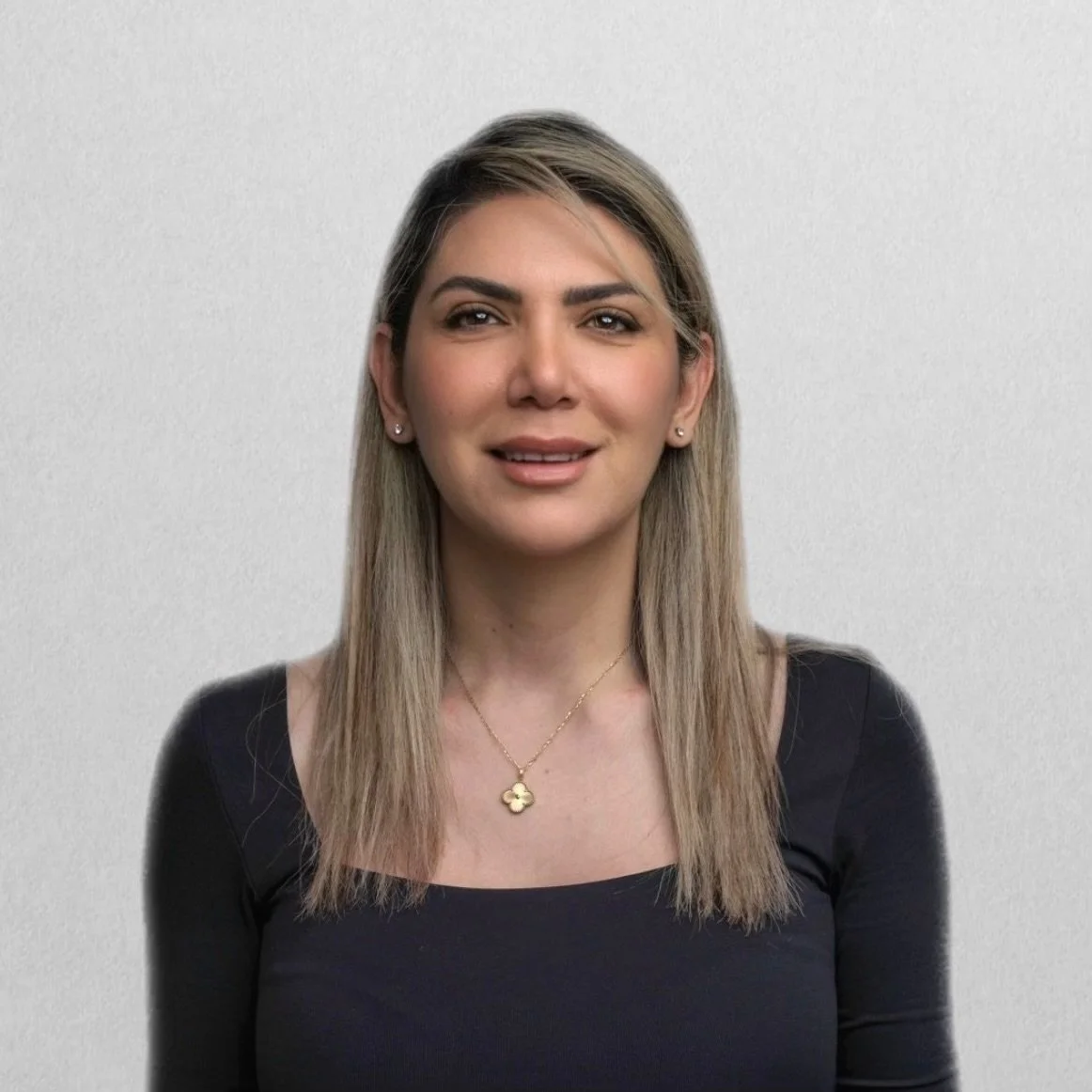 A woman with shoulder-length brown hair and red lipstick sitting indoors, holding a bouquet of white and purple flowers, wearing a sleeveless white top and a gold watch.