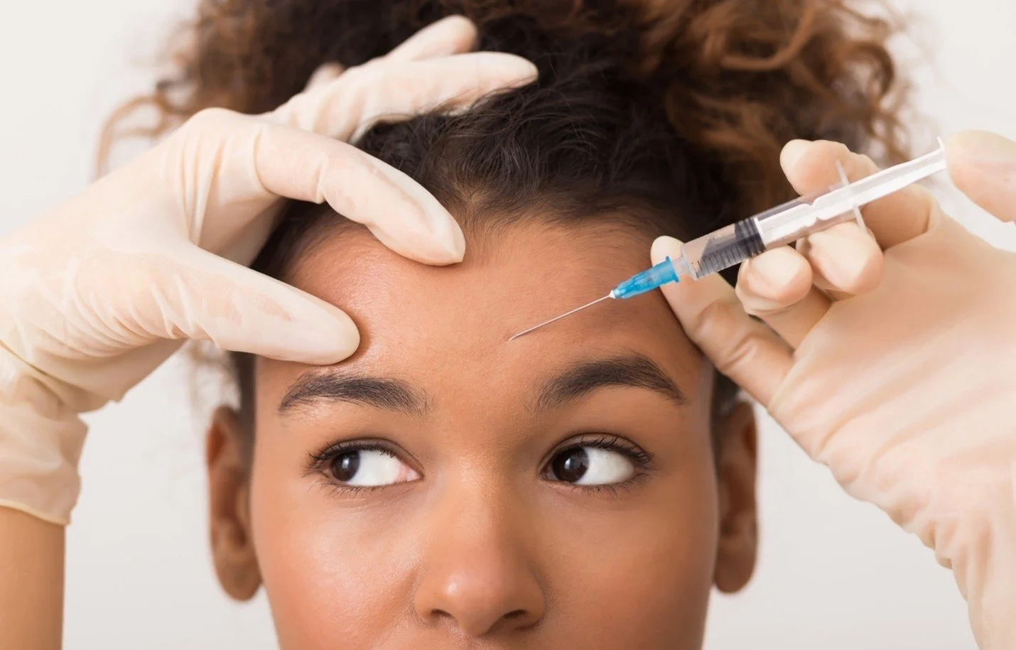 A woman receiving a Botox injection in her forehead from a healthcare professional wearing gloves.