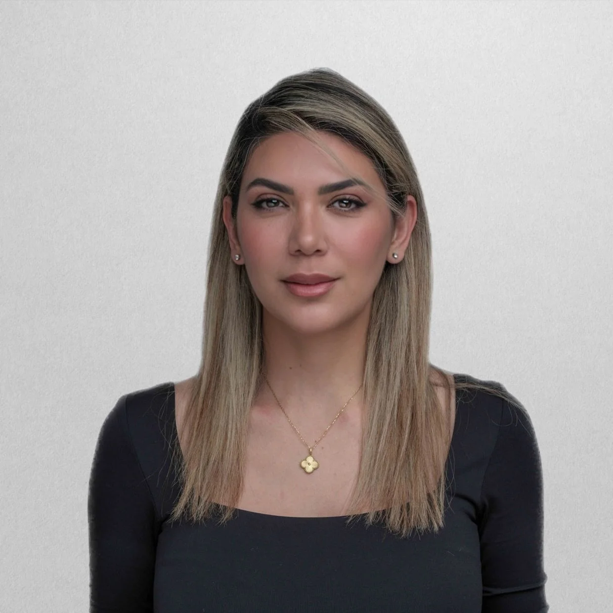 A woman with shoulder-length brown hair and red lipstick sitting indoors, holding a bouquet of white and purple flowers, wearing a sleeveless white top and a gold watch.