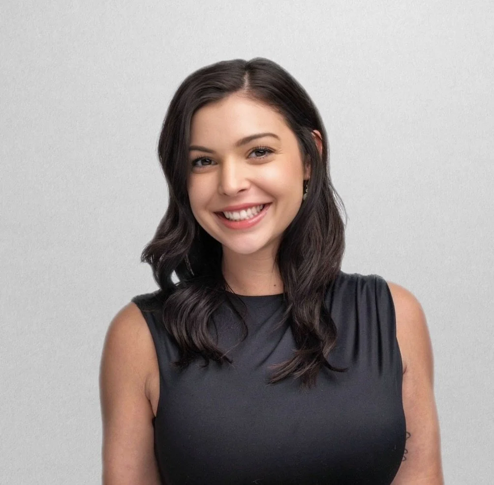 A young woman with long wavy brown hair smiling in a black medical uniform.