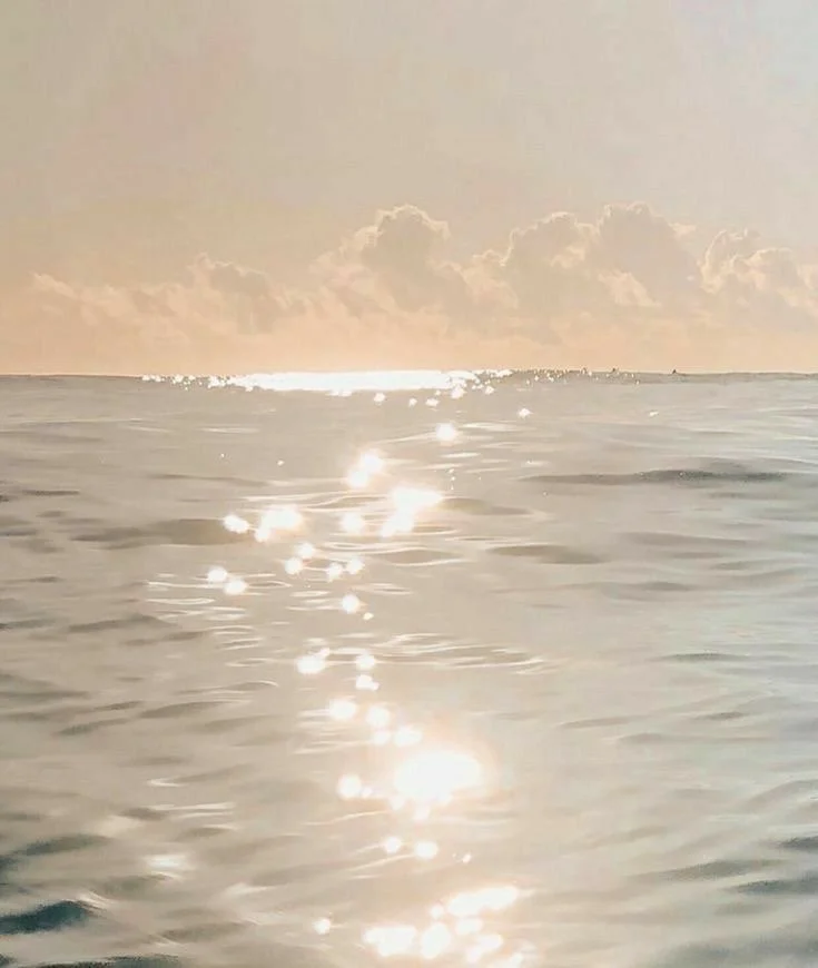 Sunset over the ocean with reflections on the water surface and clouds in the sky.