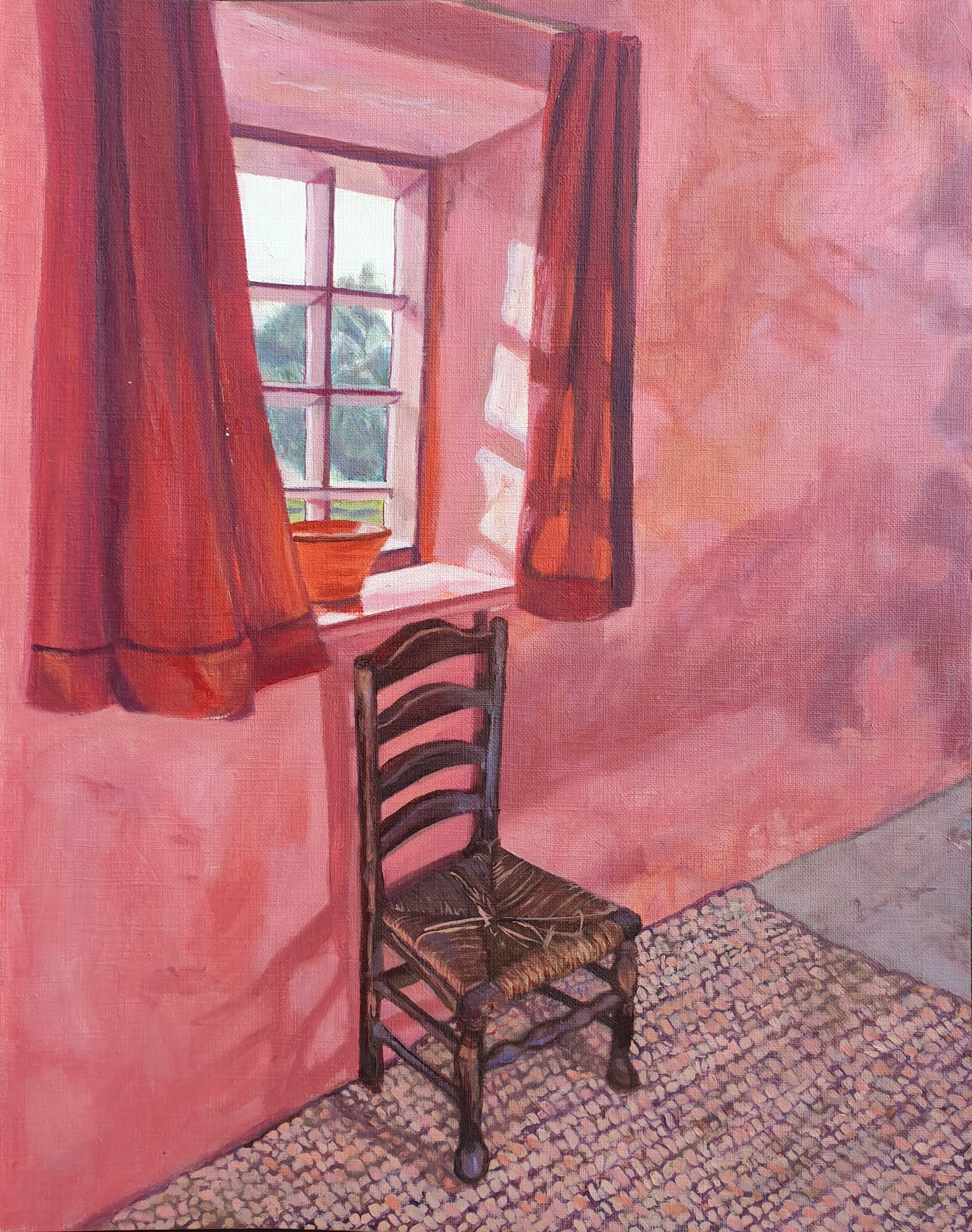 A wooden dining chair against a pink wall, under an old sash window with red curtains. Rag rug on concrete floor.