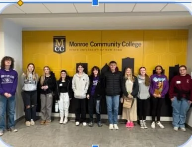 Group of students standing in front of a Monroe Community College sign at State University of New York.