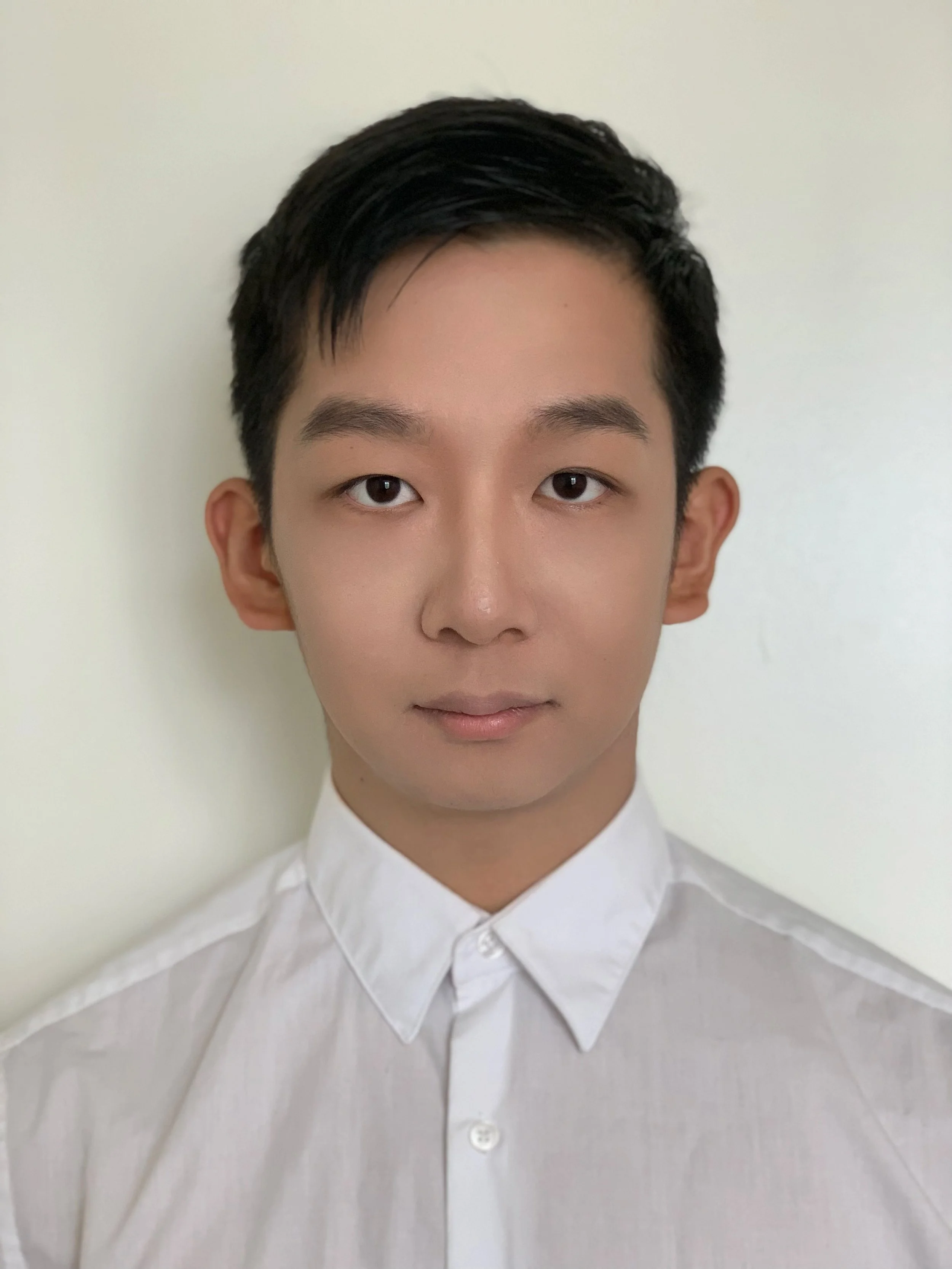 A young man with short black hair wearing a white button-up shirt, looking at the camera against a plain white background.