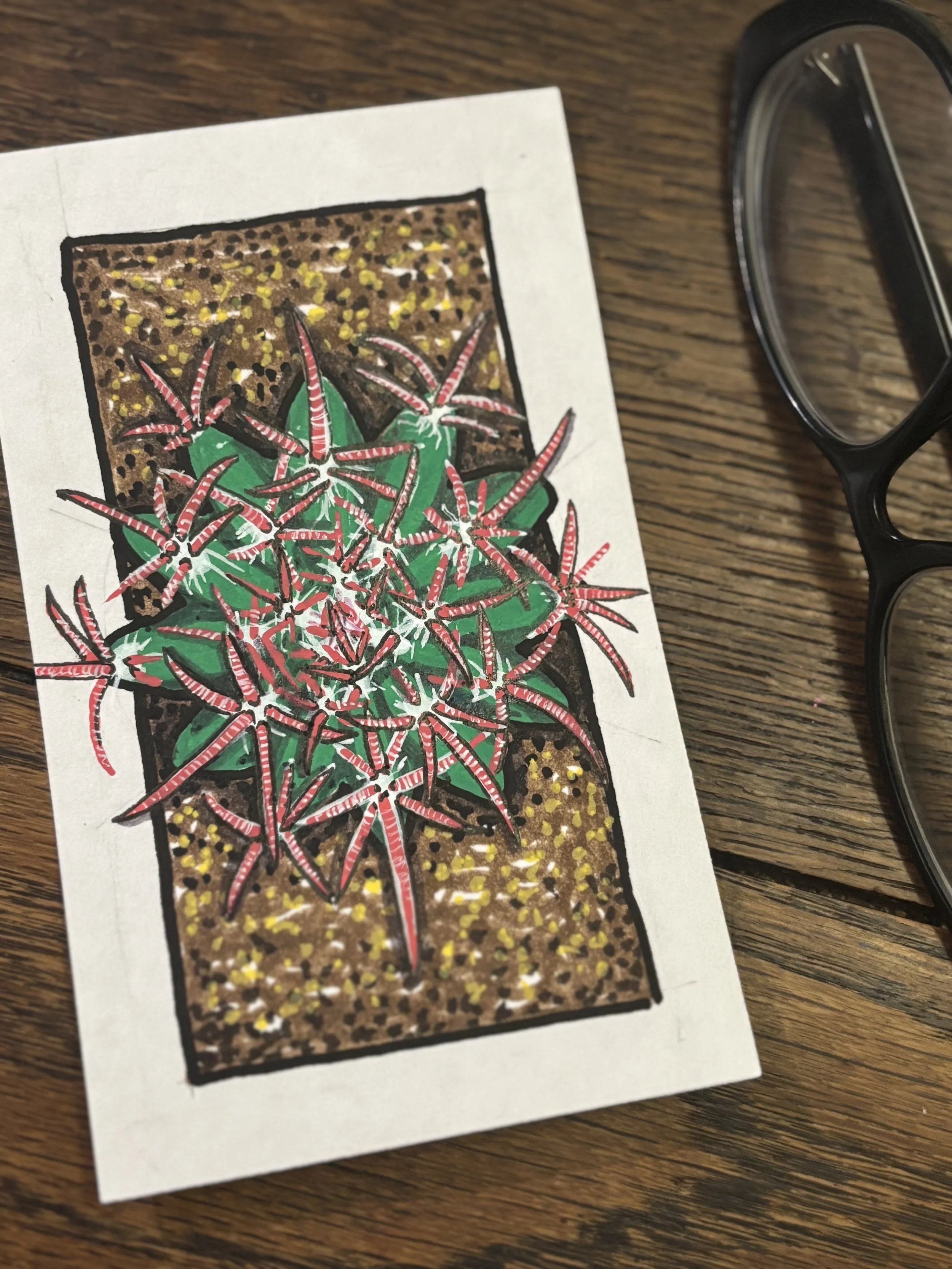 A drawing of a potted cactus with red and white spines on a wooden surface, next to a pair of black-framed glasses.
