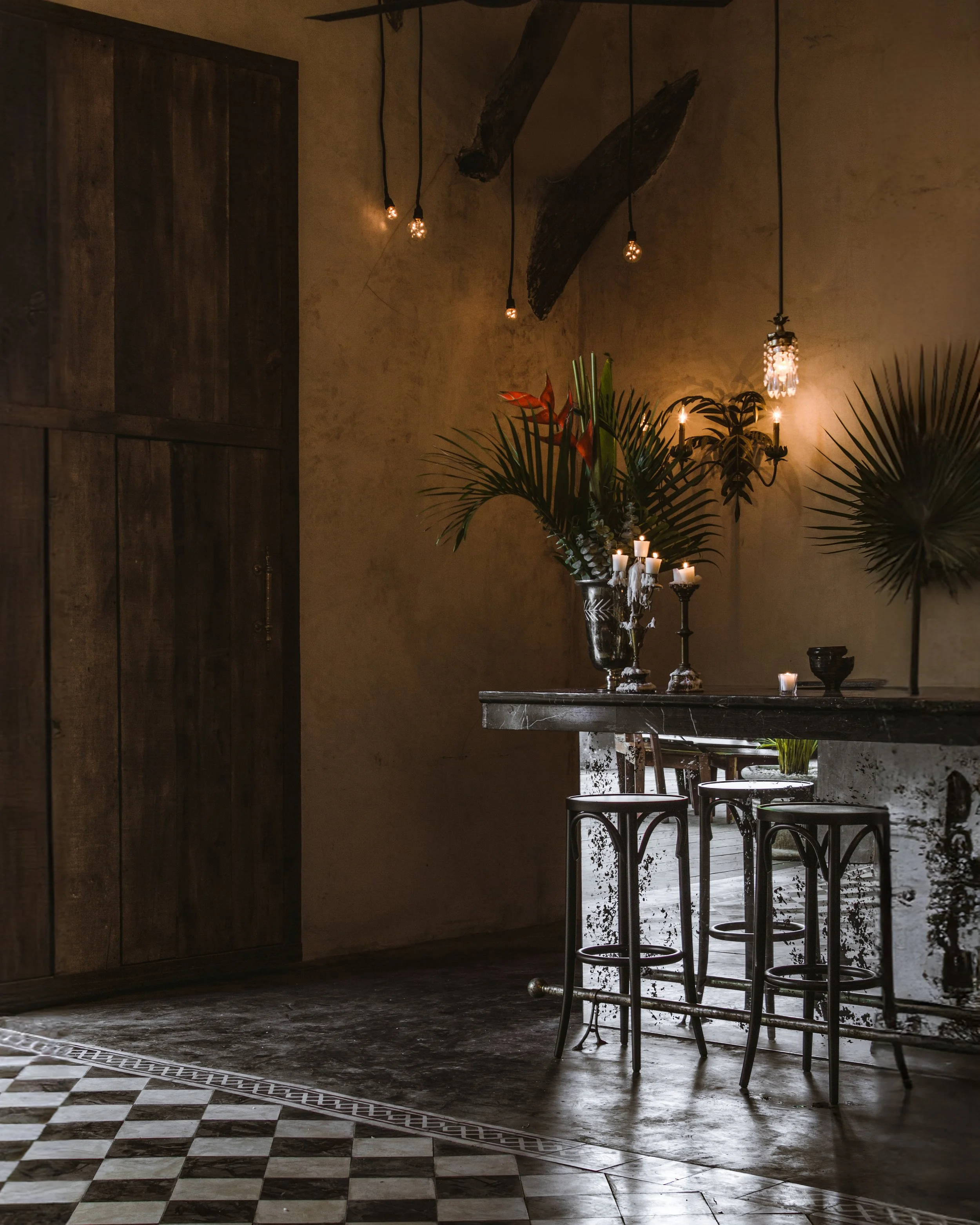 Interiores elegantes con mesa de mármol, plantas verdes, candelabros con velas y luces colgantes con estilo vintage.