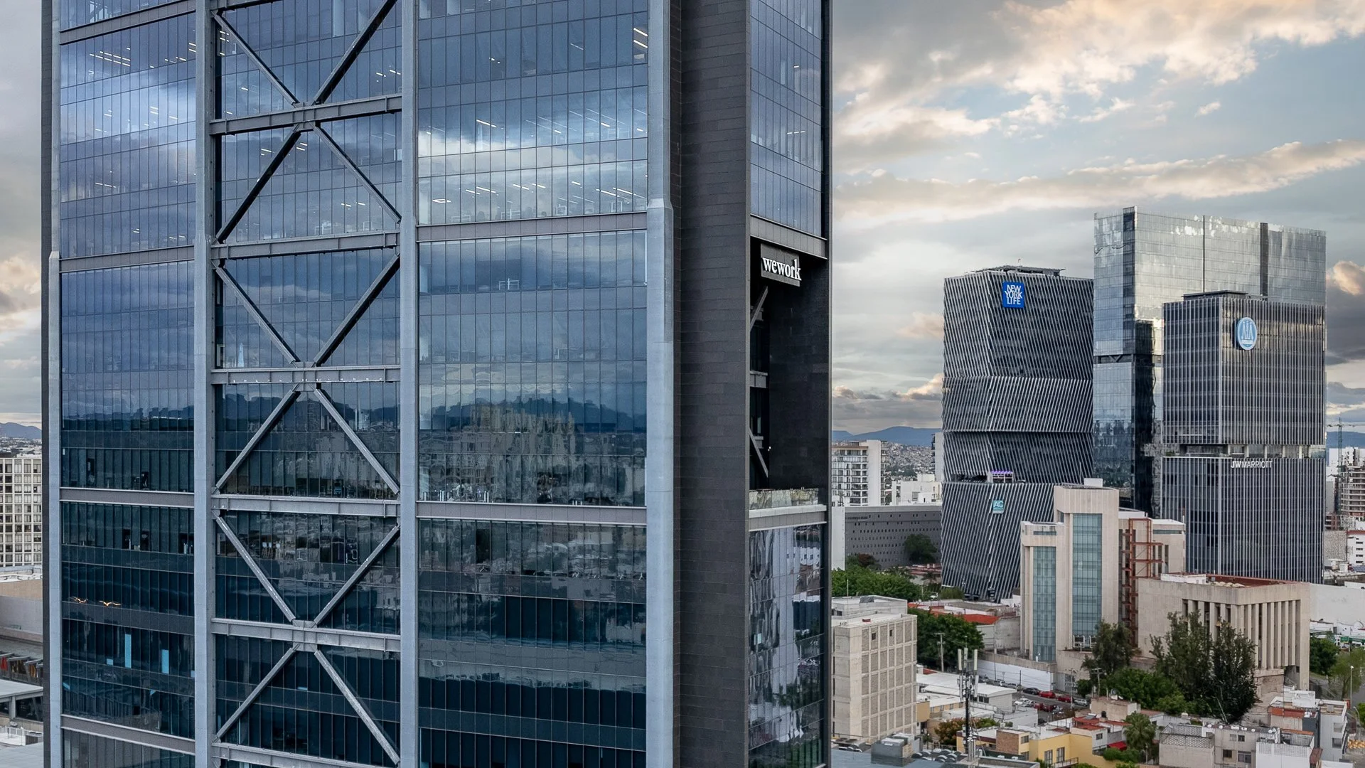 Vista de una ciudad con edificios modernos de gran altura y fachadas de cristal, en un día parcialmente nublado.