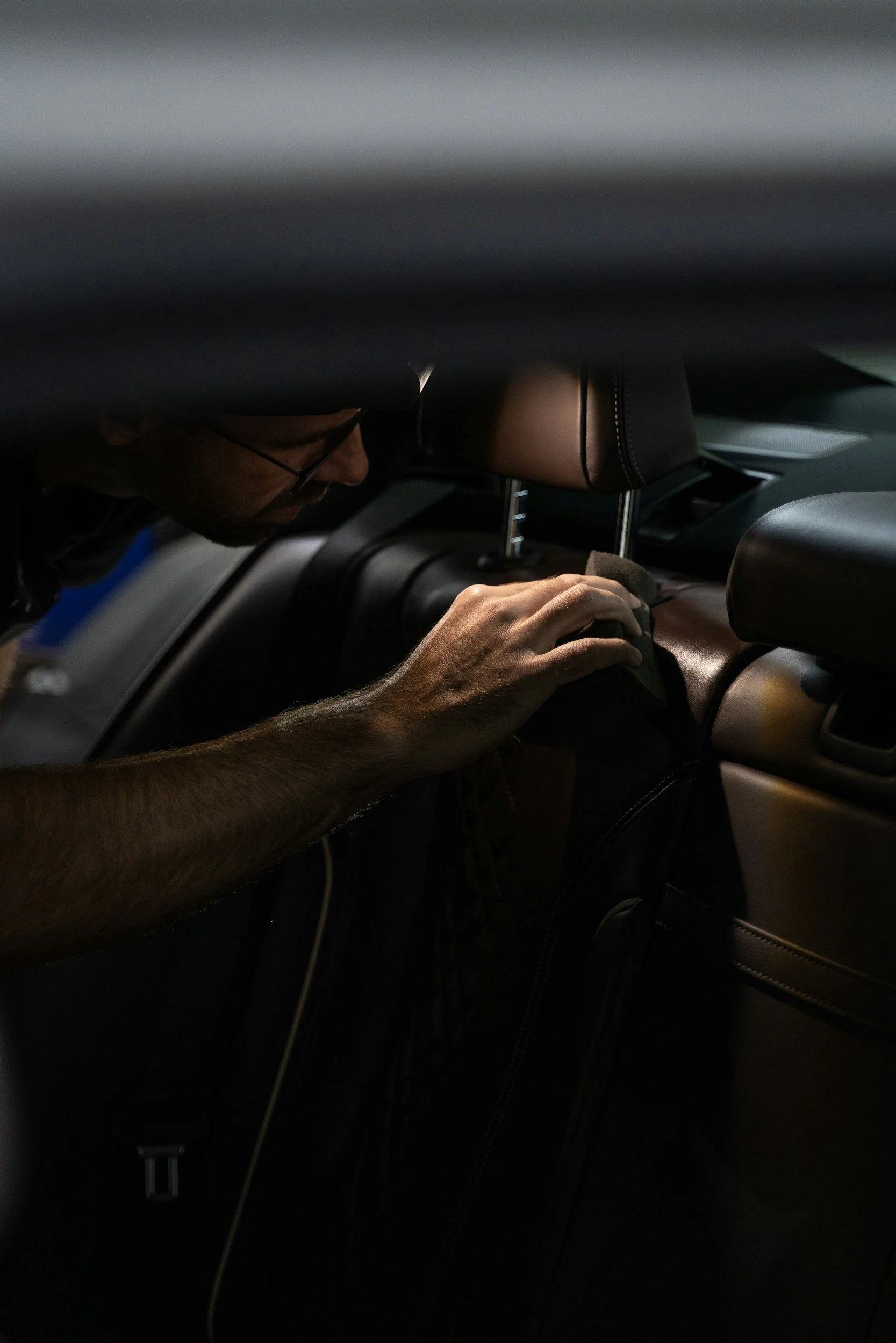 A man cleaning the interior of a car with a cloth, focusing on the dashboard area.