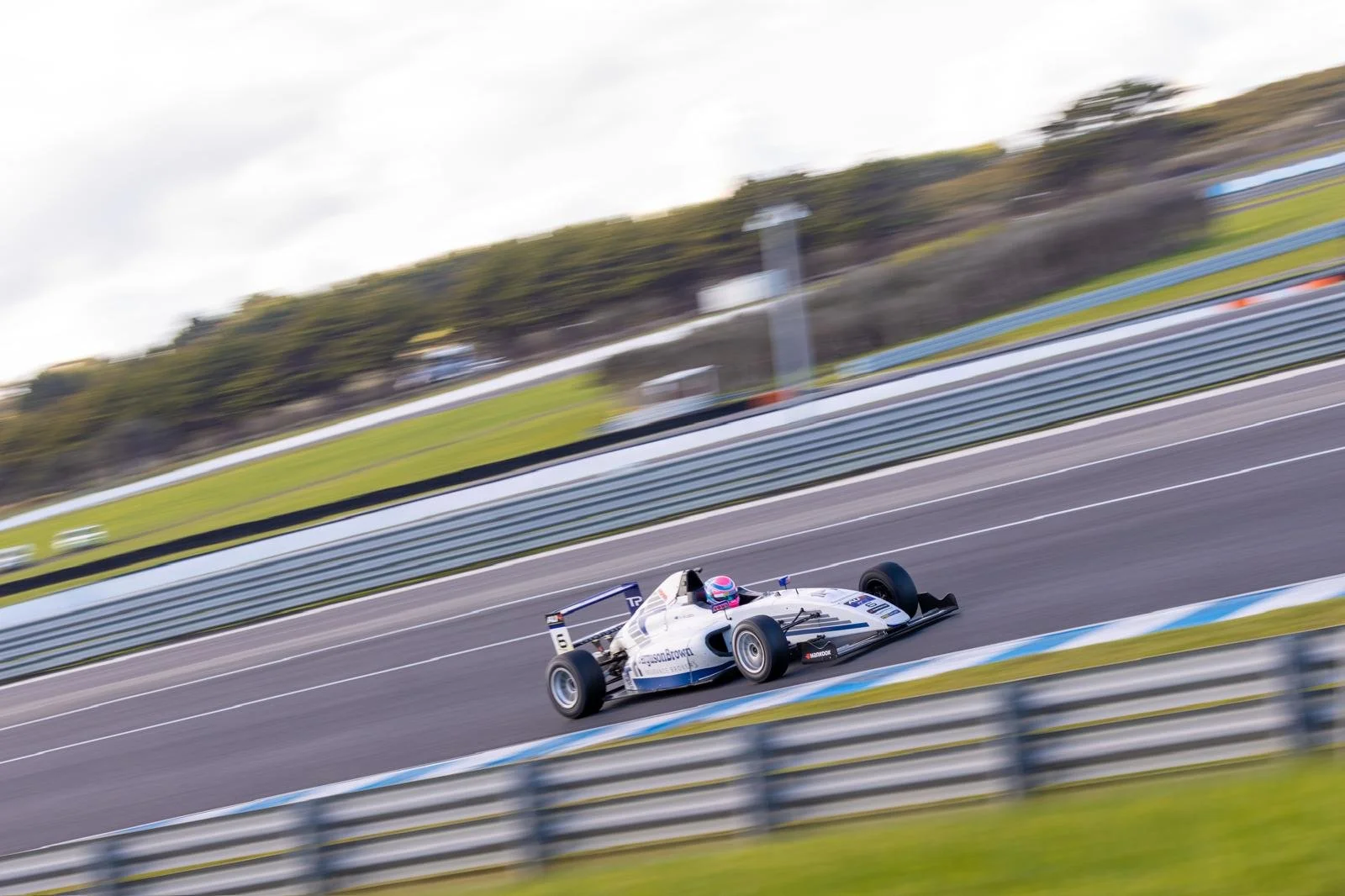 A race car with a pink helmet speeding on a race track with blurred background.