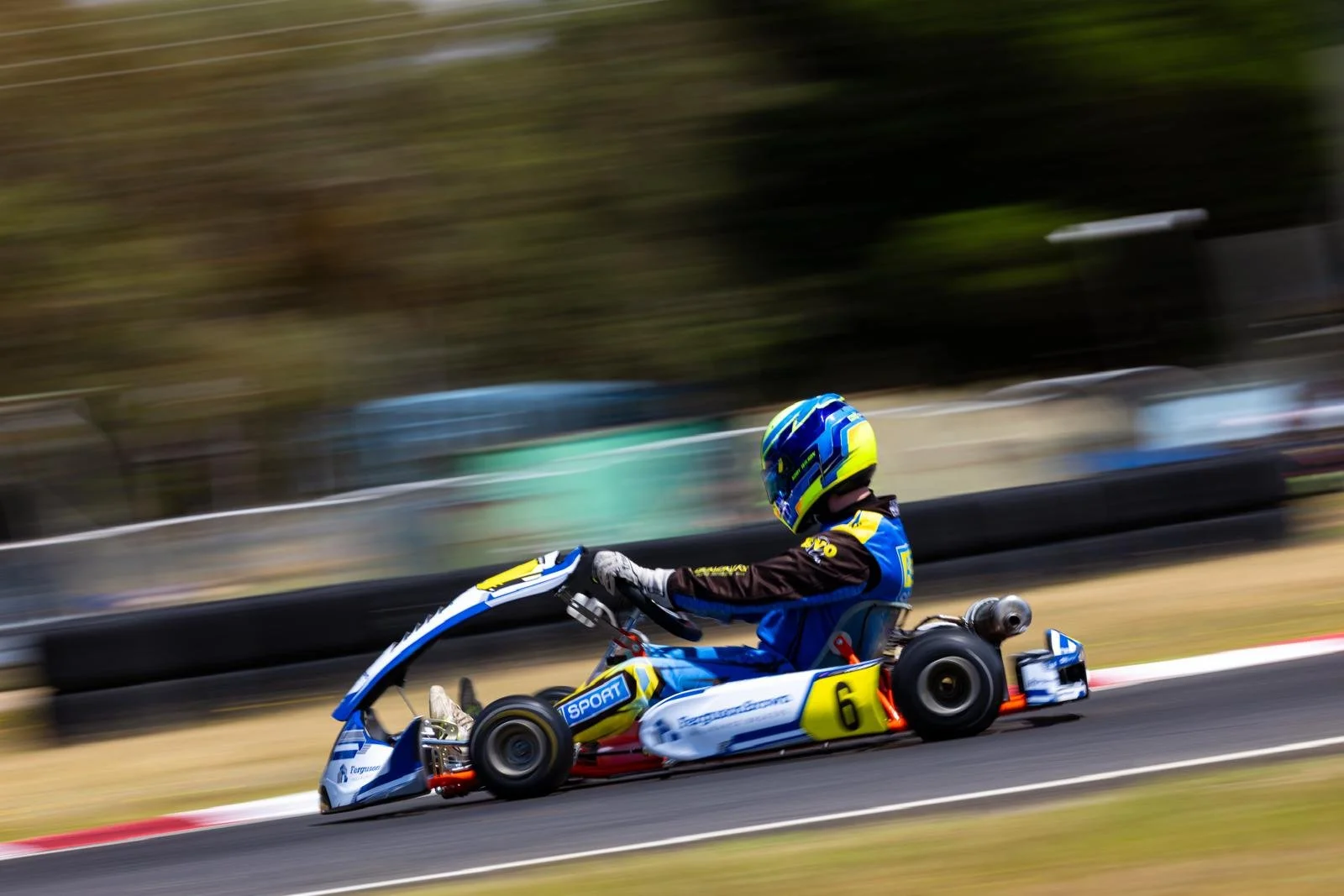 Go-kart racer wearing a helmet and racing suit driving on track with blurred background.