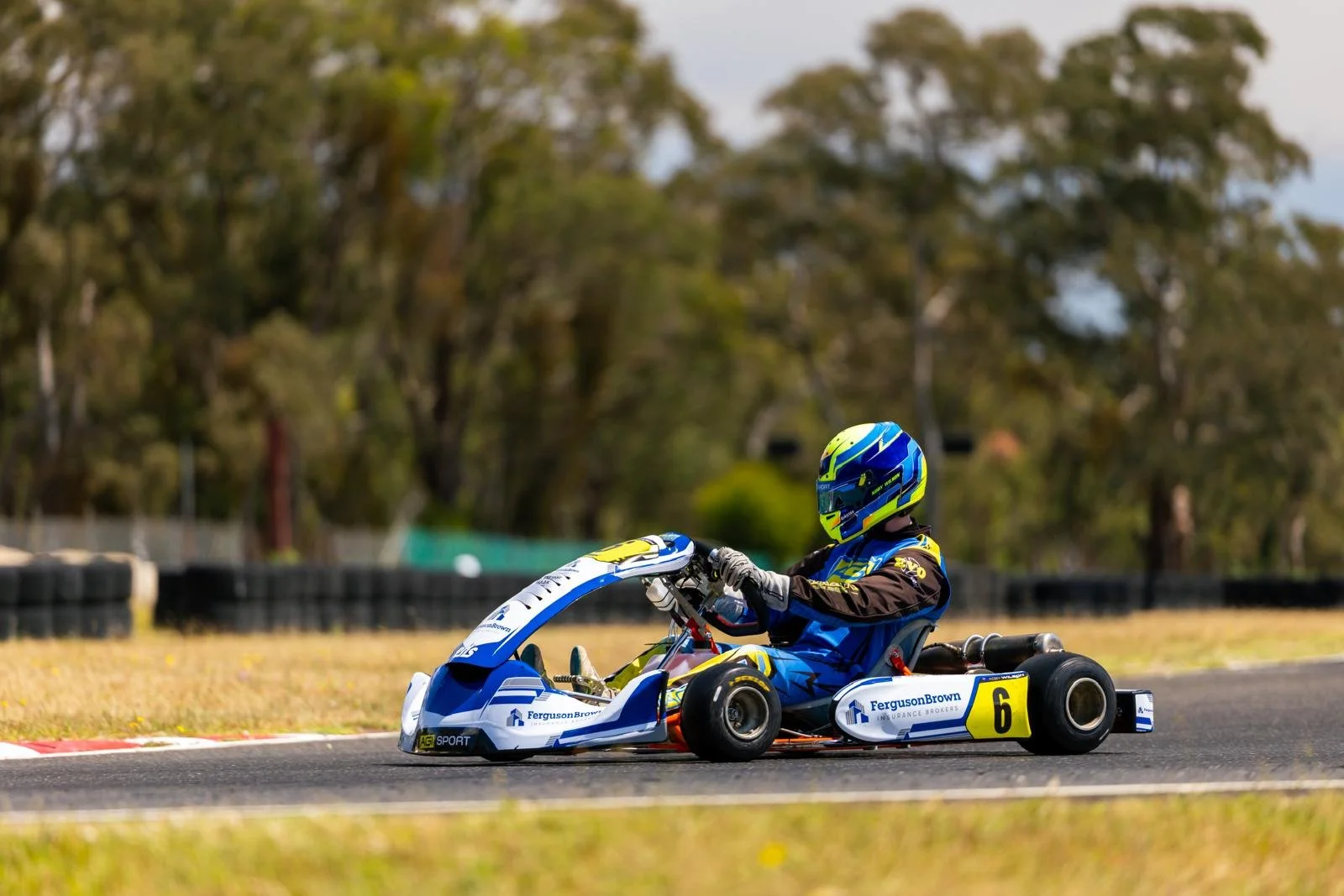 Go-kart racer in blue and yellow gear navigating a turn on the track.