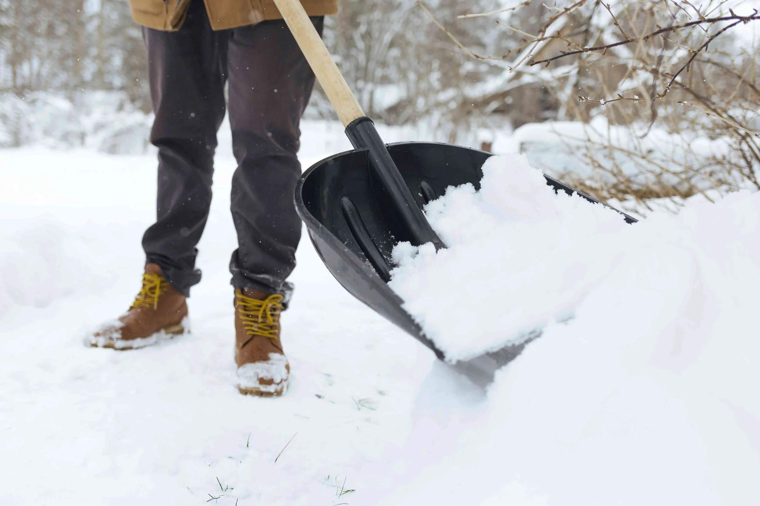 Person shoveling snow with a black snow shovel in a winter landscape.