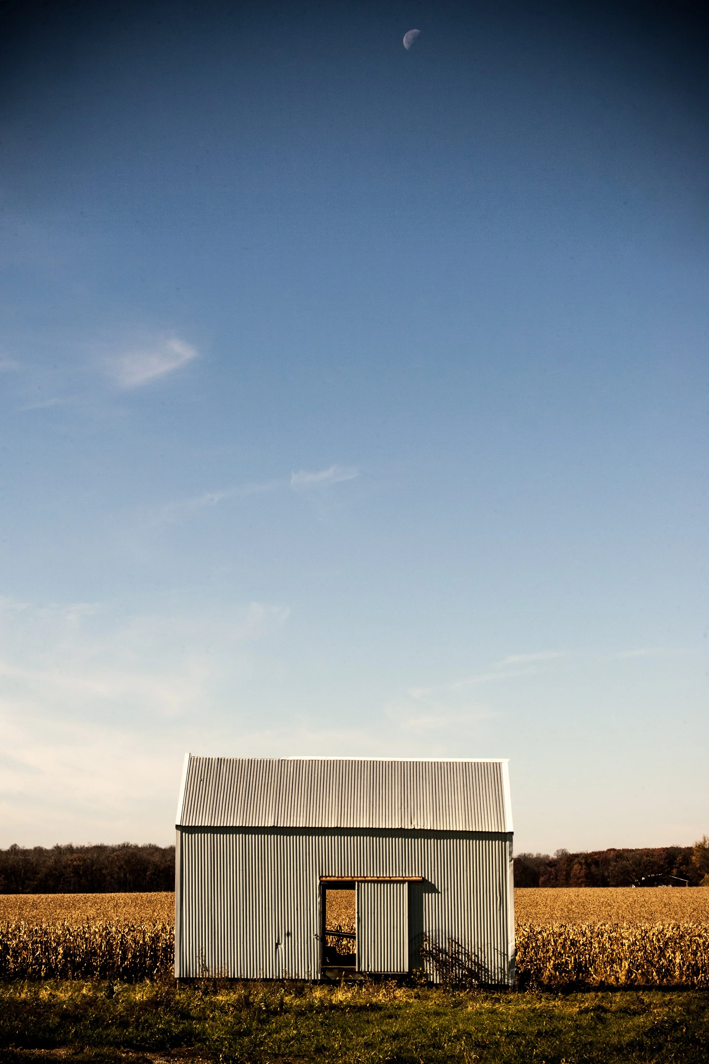 A small metal shed in a field with a clear sky above and a crescent moon visible in the top corner.