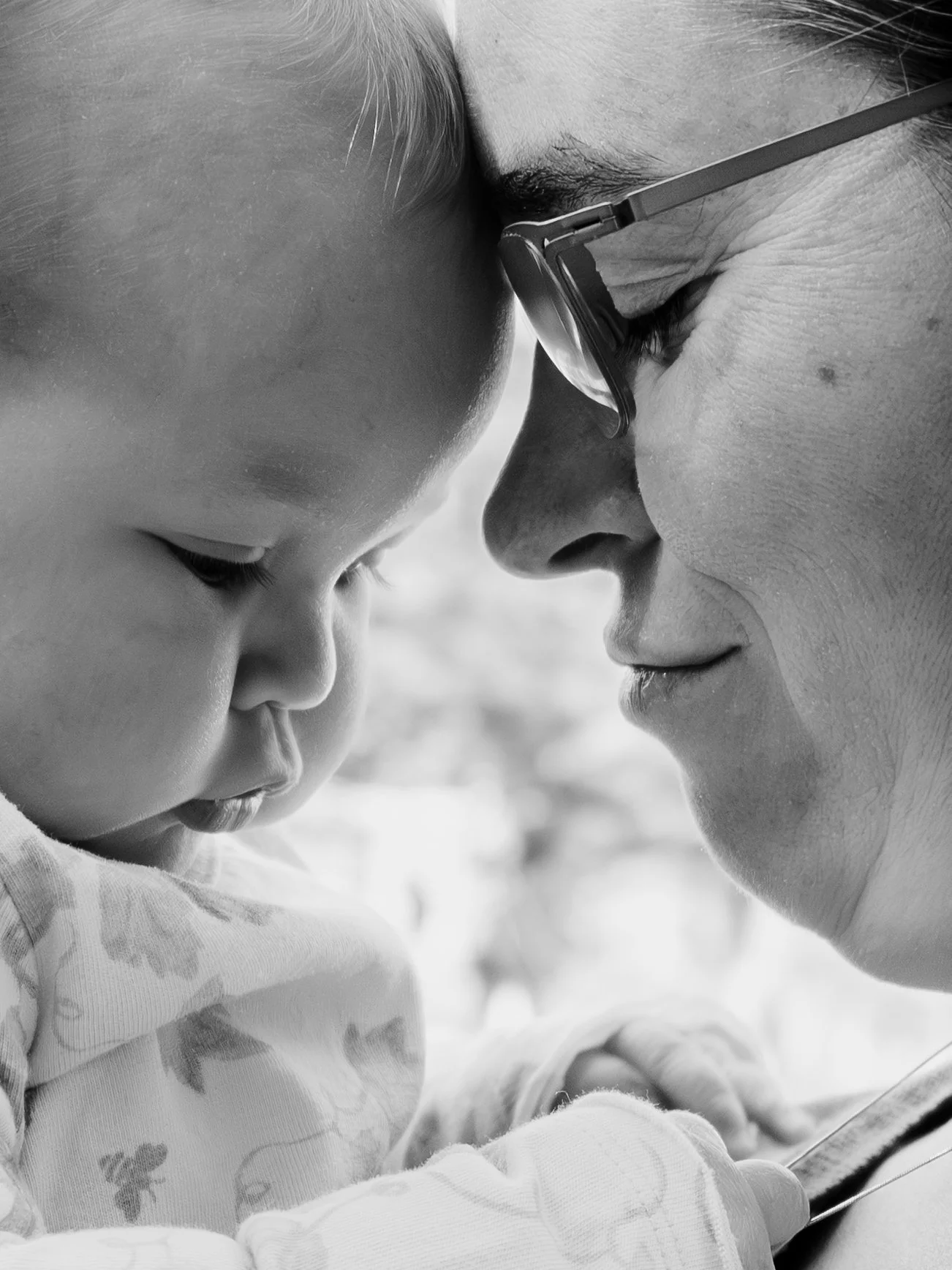 A close-up black and white photo of an adult woman and a young child touching foreheads, with their eyes closed, smiling gently.