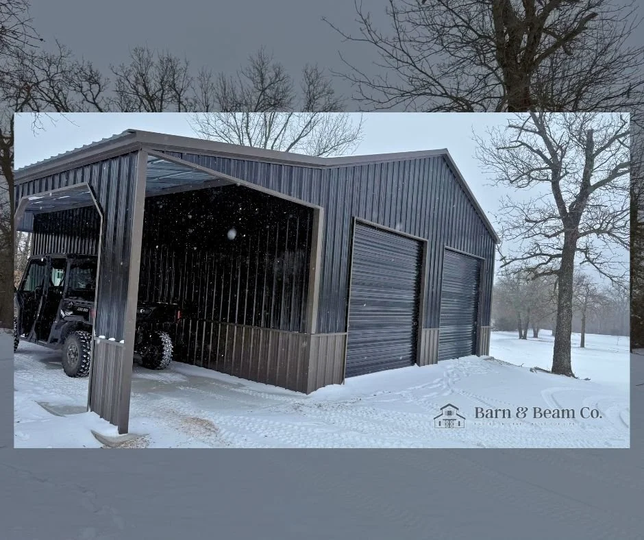 A black metal barn with two garage doors in a snowy landscape with leafless trees, branded with Barn & Beam Co.