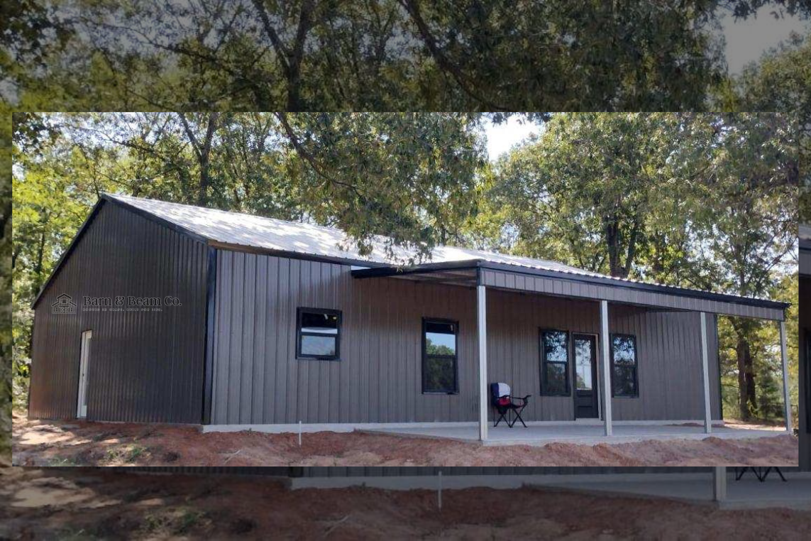 A modern metal building with a covered porch, three windows and a door, surrounded by trees and dirt ground.