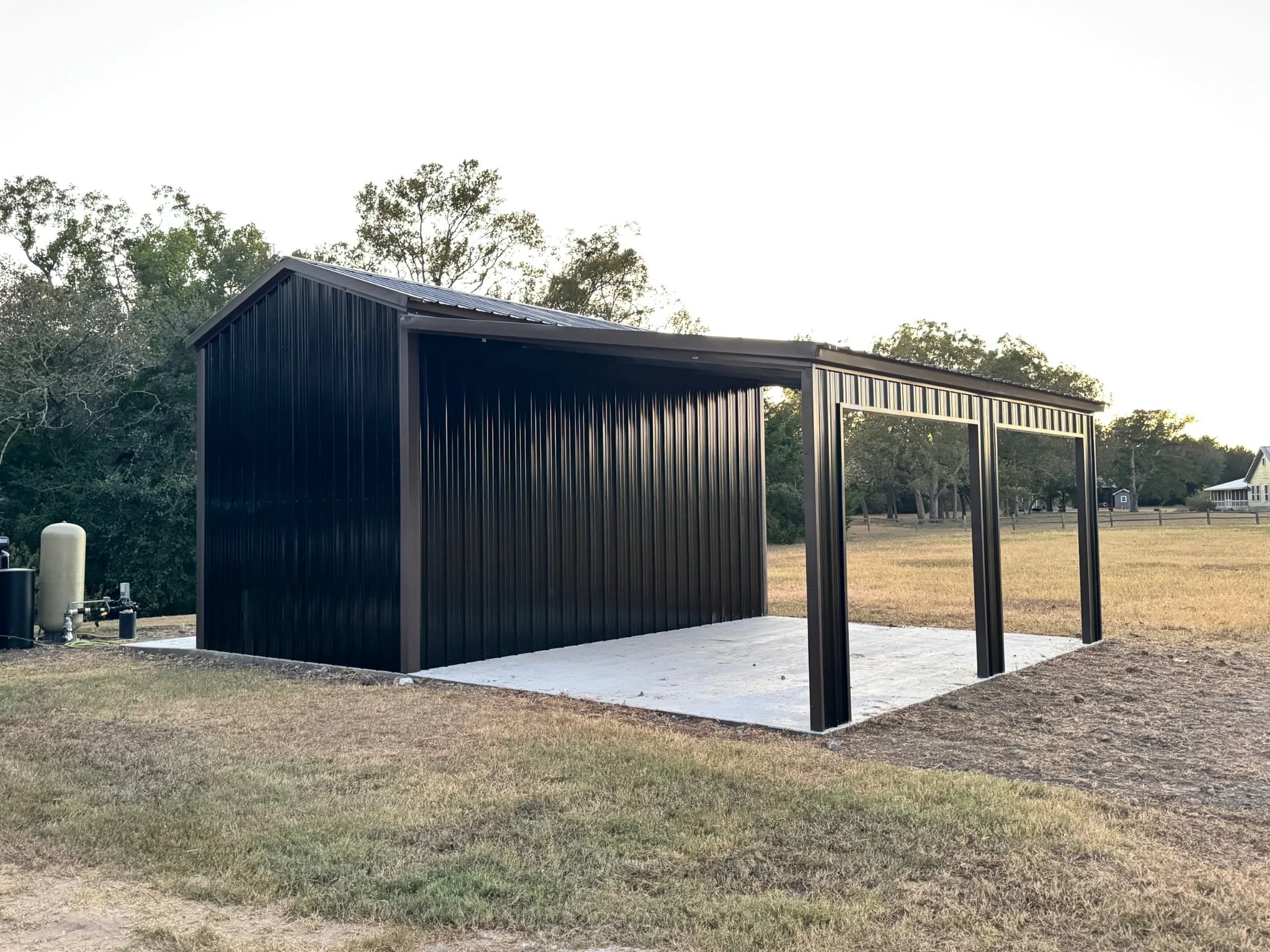 A black metal carport with a lean to roof located on a concrete slab