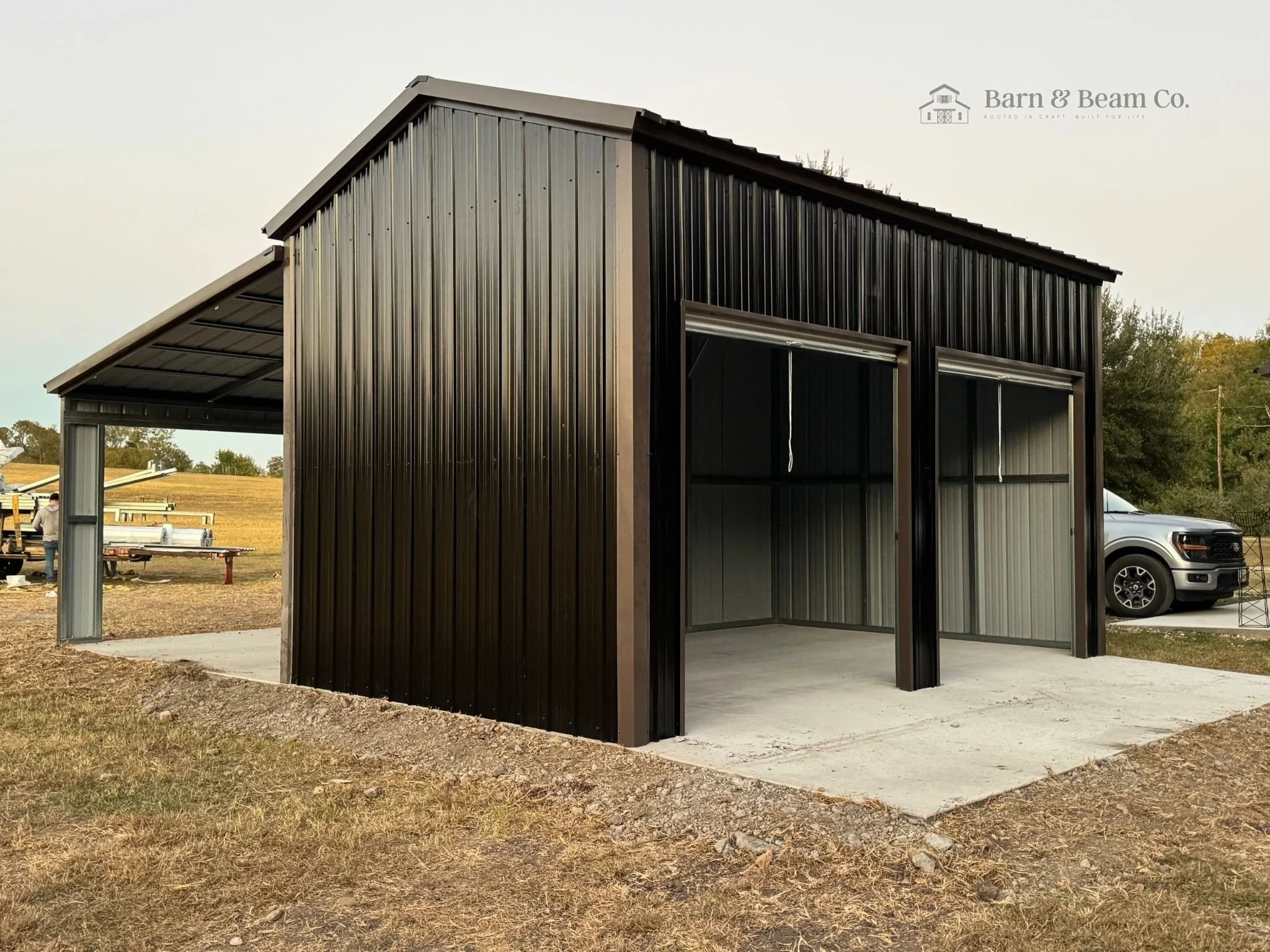 Black metal shed with open garage doors on a concrete pad in an outdoor yard.