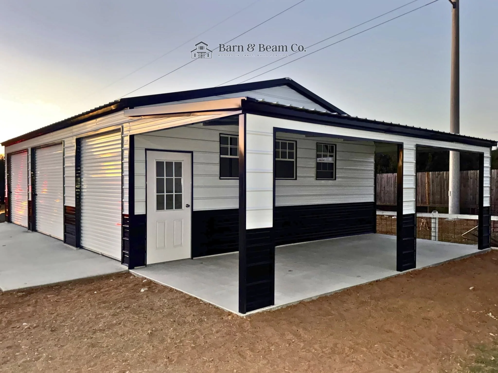 A metal building with a white exterior, black trim, and a small door with a window, situated on a concrete slab outside.