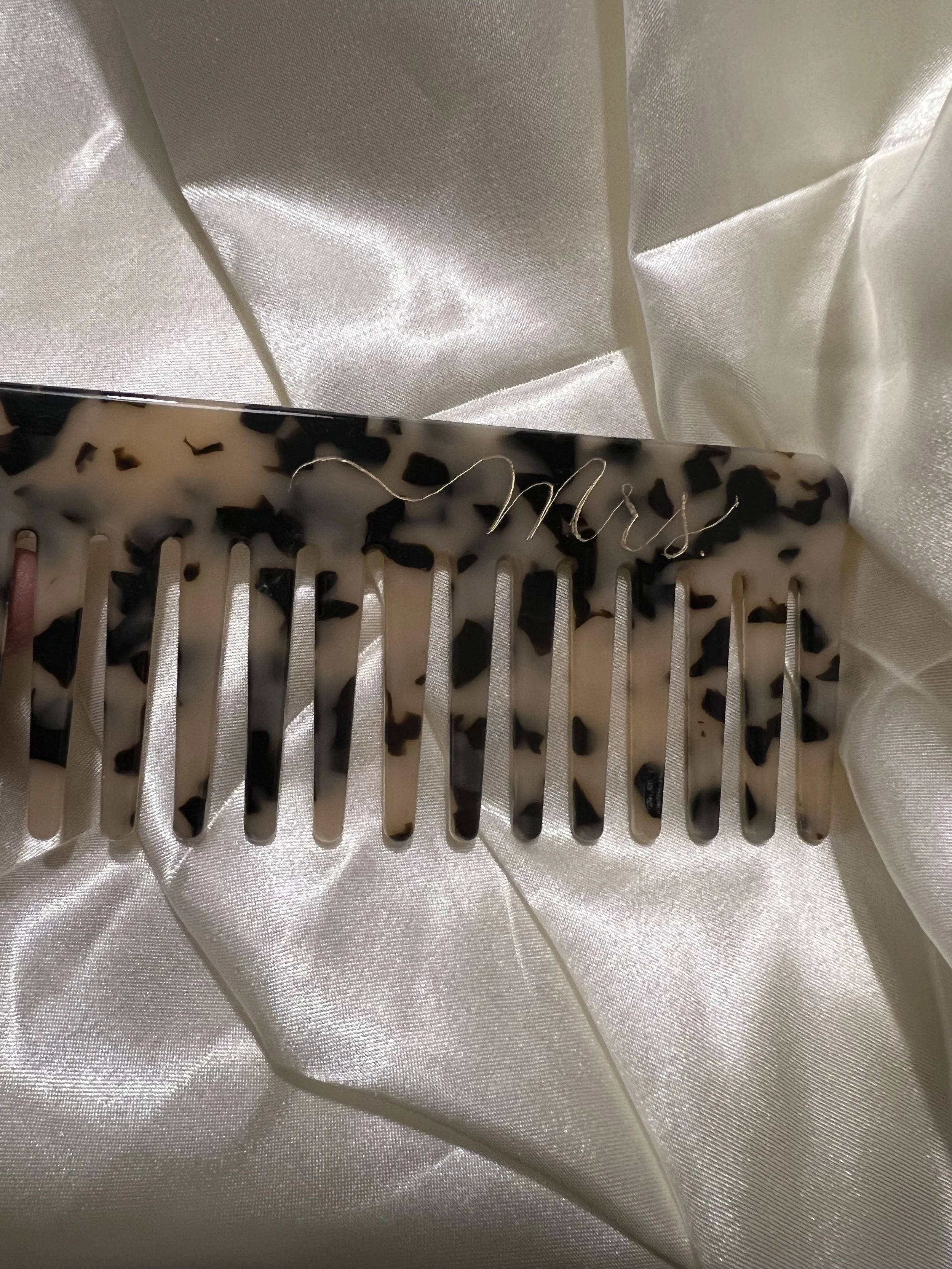 bridal, bridesmaid gift, personal, unique , beautiful, pretty A decorative hair comb with a tortoise shell pattern and the word 'Mrs.' written in gold cursive on top, resting on satin fabric.